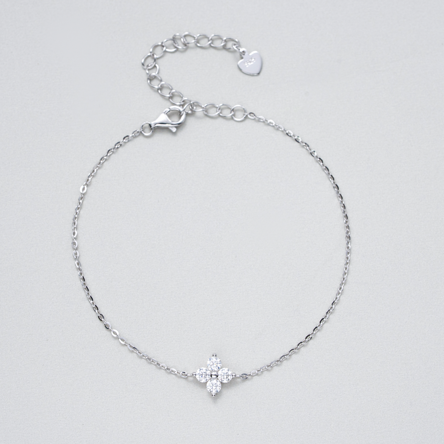 A delicate silver chain bracelet with a small silver cross charm set with clear stones, displayed on a light gray background.