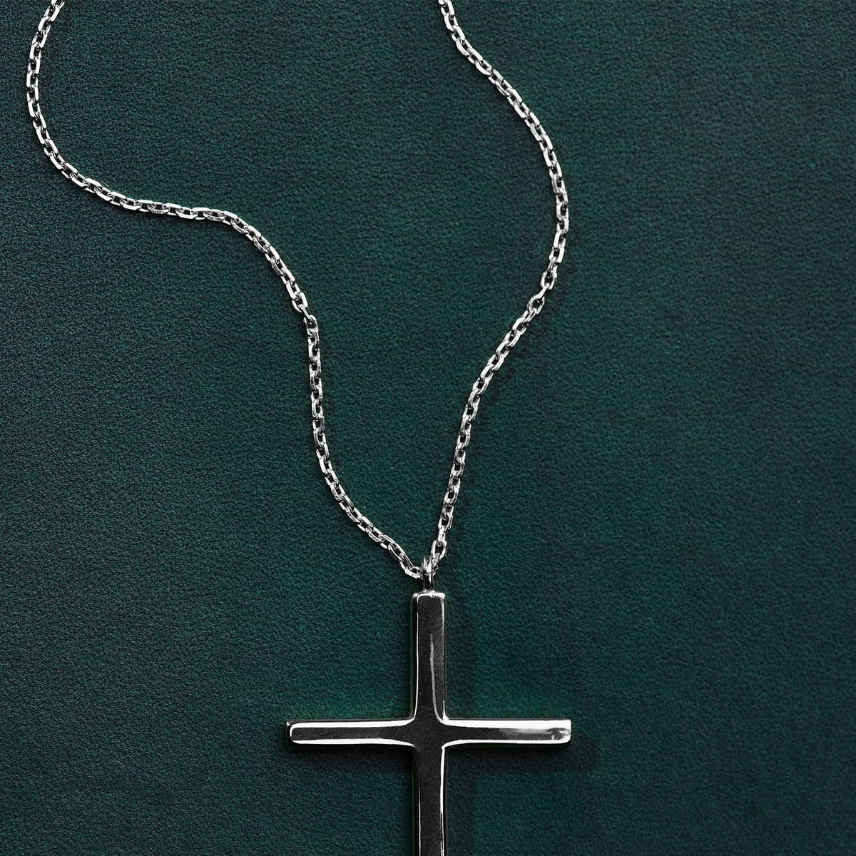 A silver cross pendant necklace on a delicate silver chain, displayed against a textured dark green background.