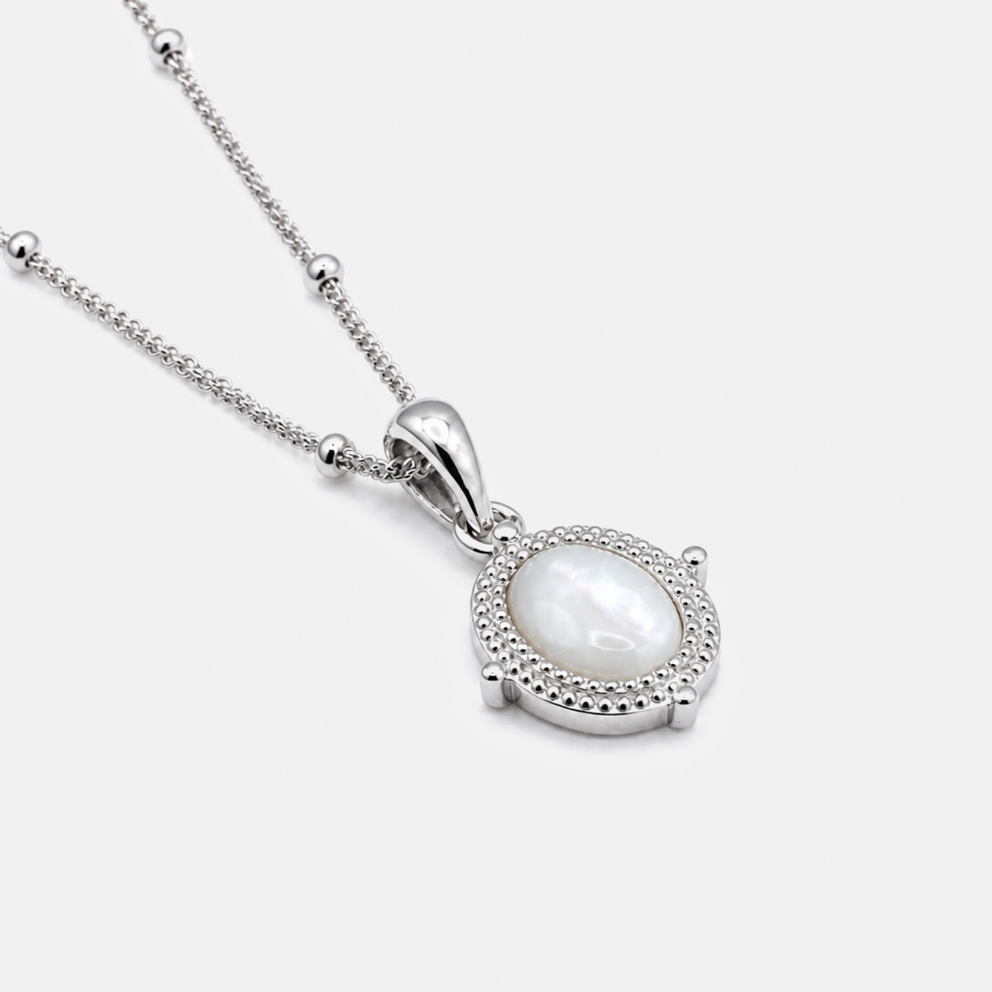 A silver pendant necklace featuring a round white mother-of-pearl center stone surrounded by a halo of small clear stones, suspended from a delicate silver chain on a light gray background.