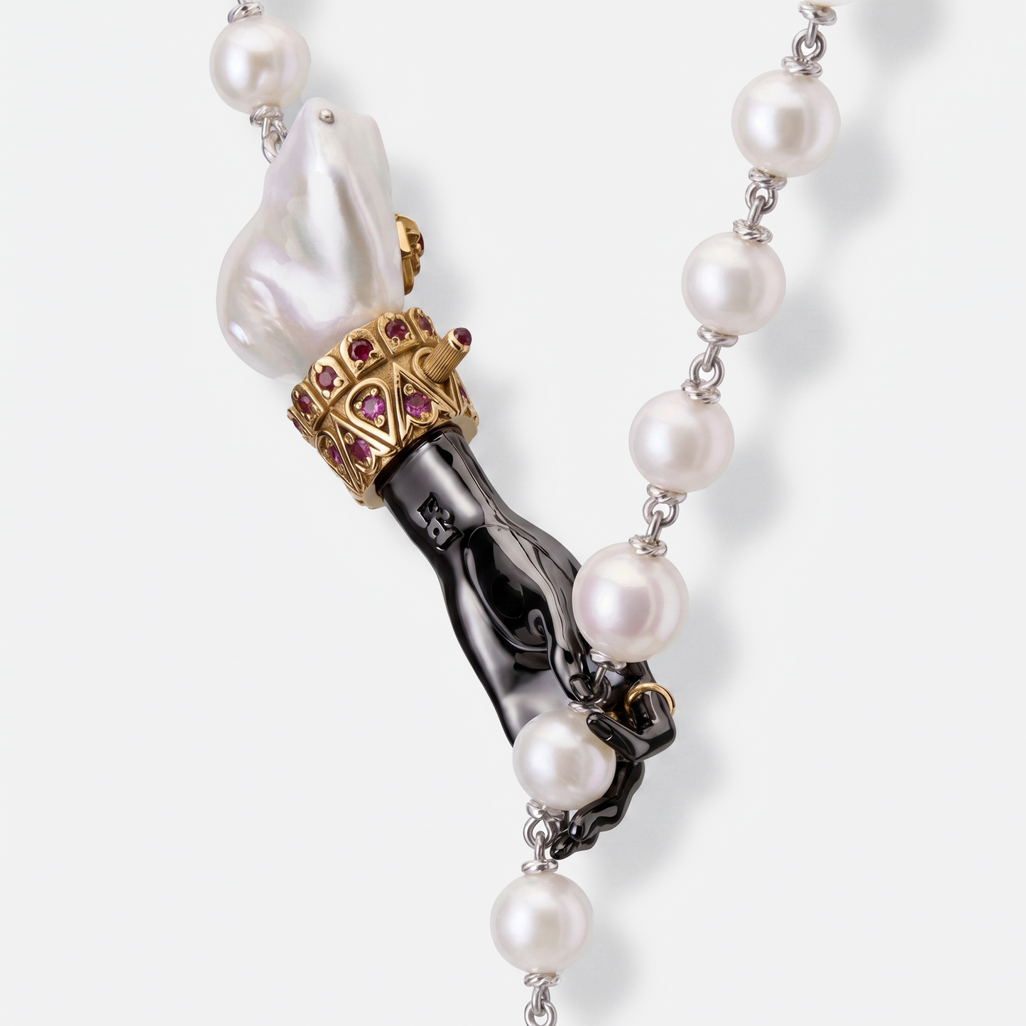 Close-up of black hand pendant with baroque pearl and gold ruby accents on pearl necklace, artistic luxury jewellery detail