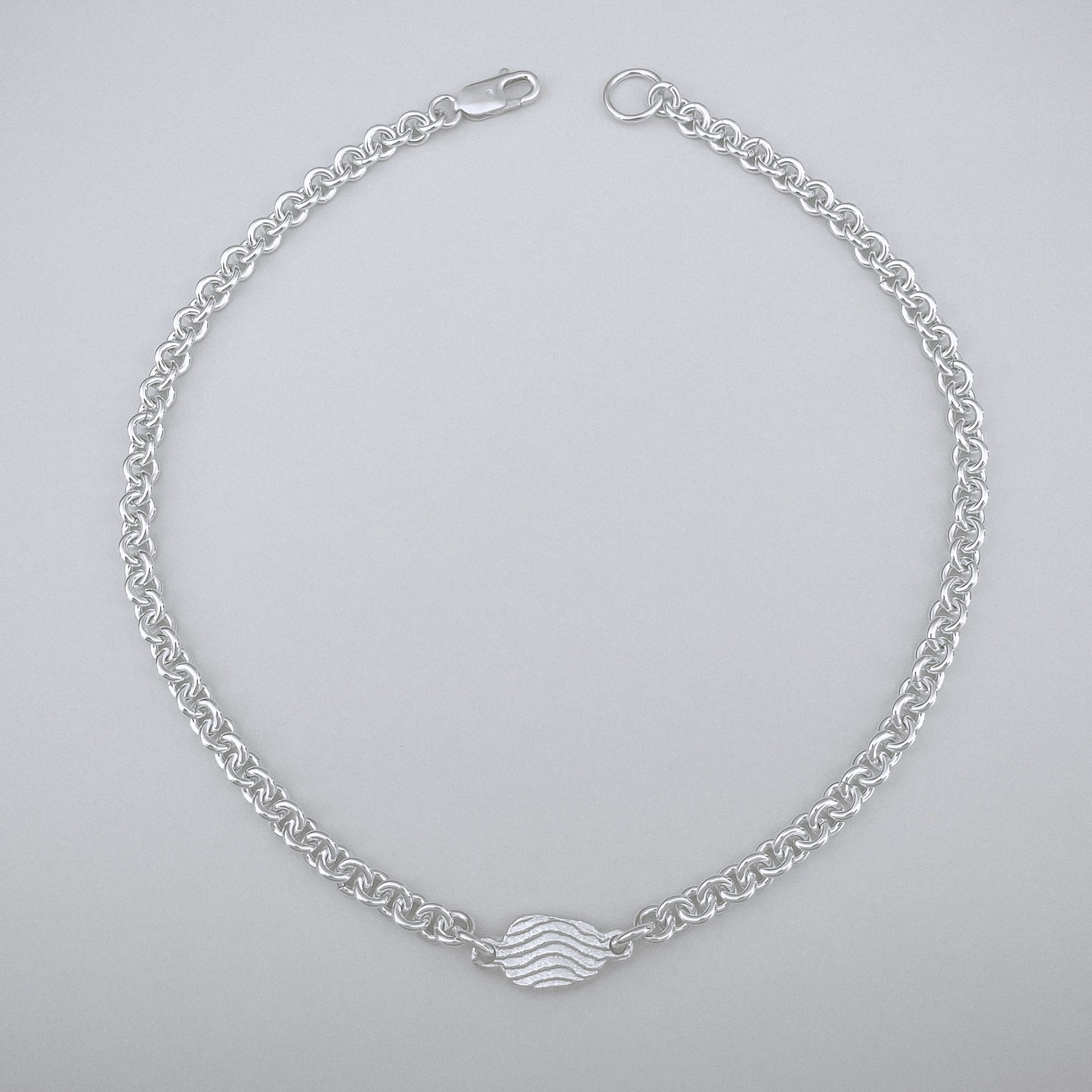 Silver chain bracelet with a wave design on a light gray background