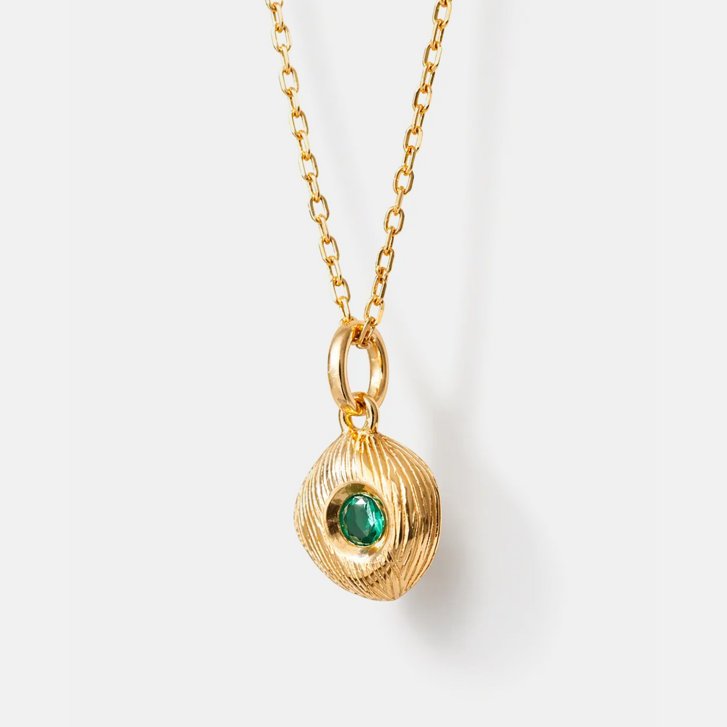 A gold chain necklace with a textured, organic-shaped gold pendant featuring a small, round green gemstone in the center, shown against a clean white background.