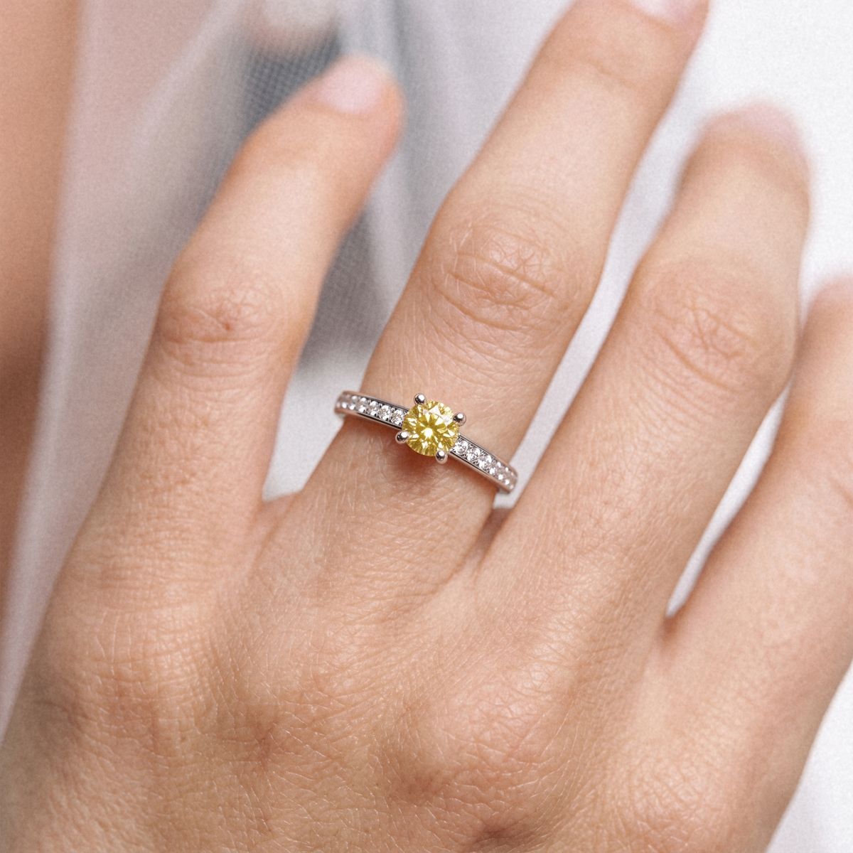 A close-up of a hand wearing a yellow diamond engagement ring with a silver-colored band set with small clear stones.