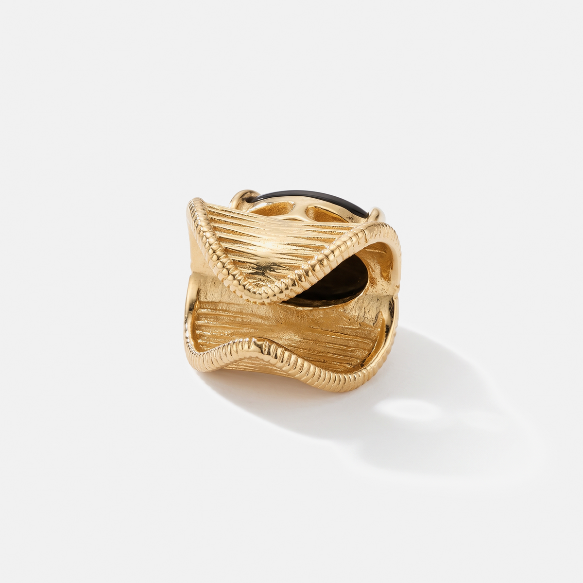 A textured gold ring with a sculptural, wavy, open design and a dark inlay, photographed on a clean white background with a soft shadow.
