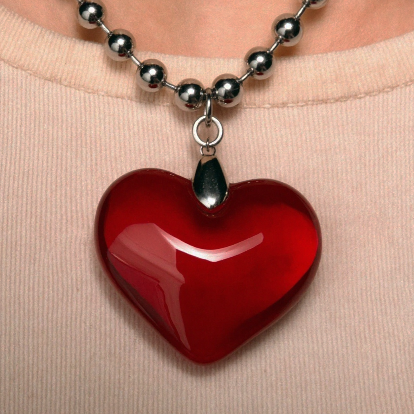 Red heart-shaped pendant on a silver chain against a beige background