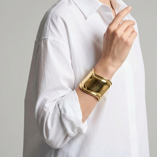 Gold bracelet worn by a person wearing a white shirt against a neutral background