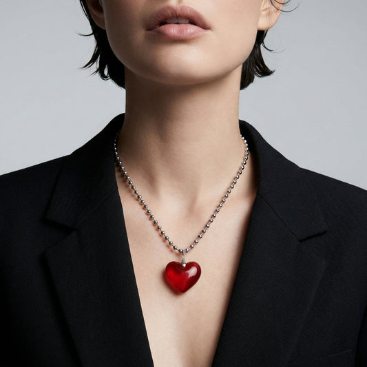 Person wearing a black blazer with a red heart pendant necklace on a gray background