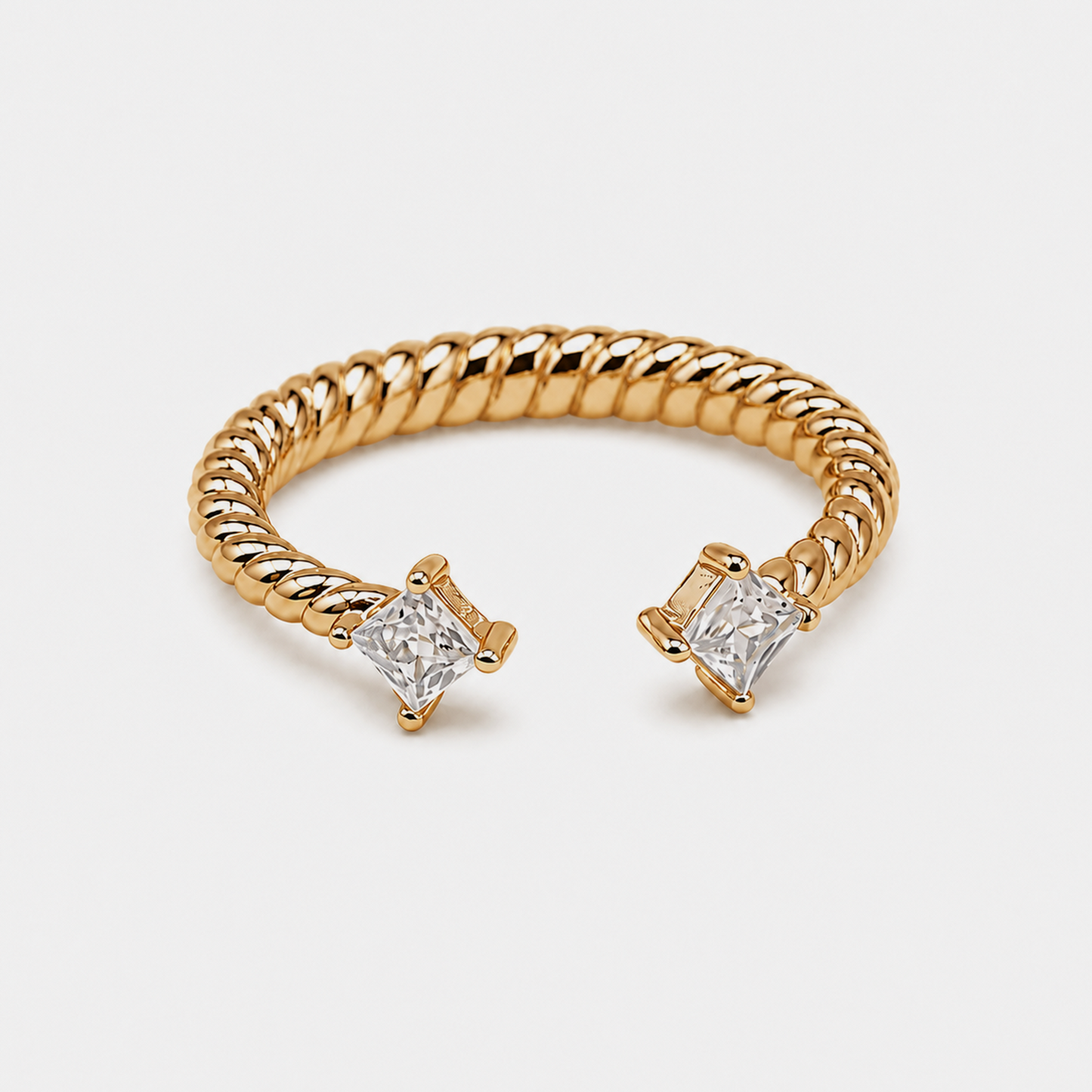 A gold rope-style cuff ring with two princess-cut clear gemstones in prong settings, shown on a light gray background.