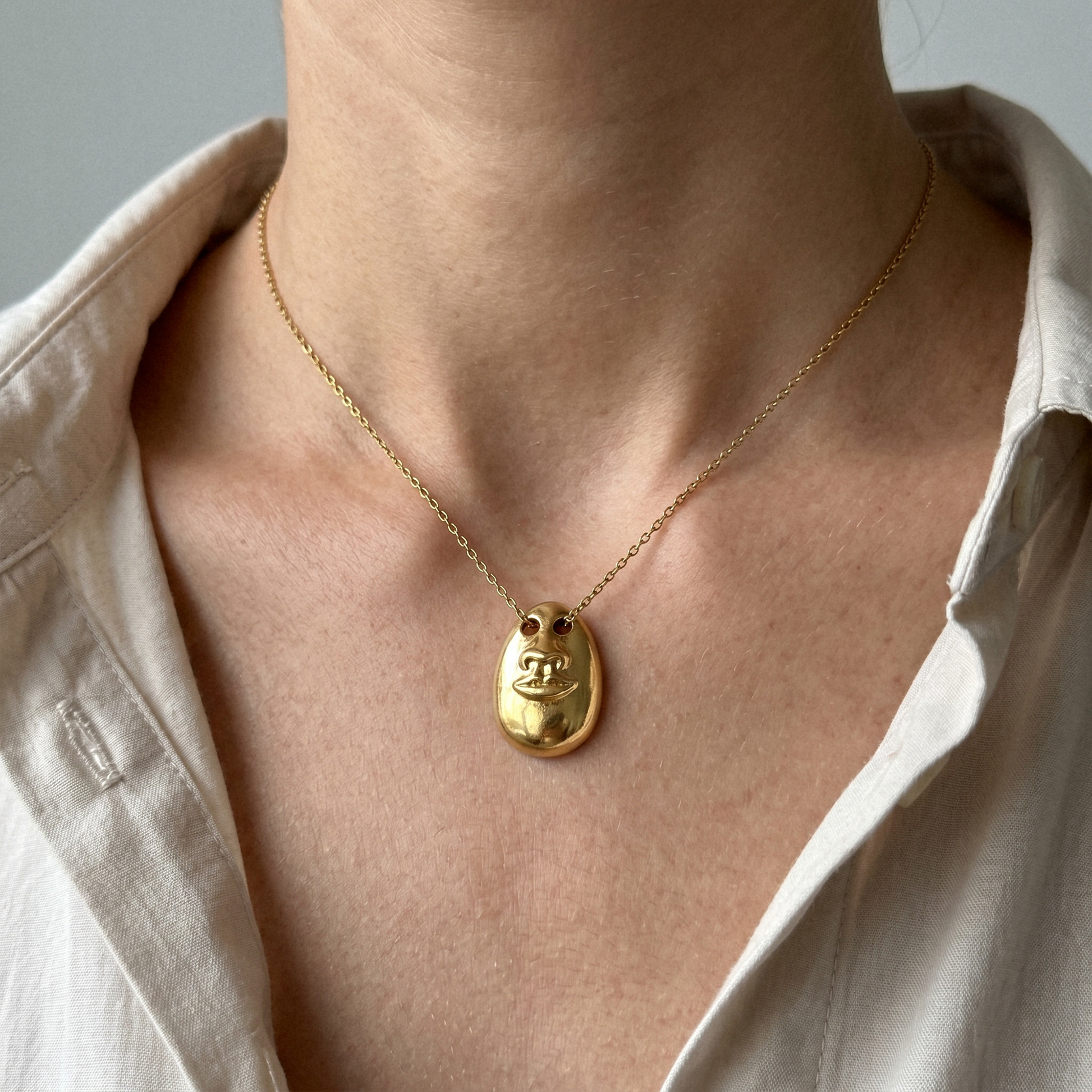 See No Evil Pendant Necklace in gold worn on a delicate chain with a relaxed beige shirt.