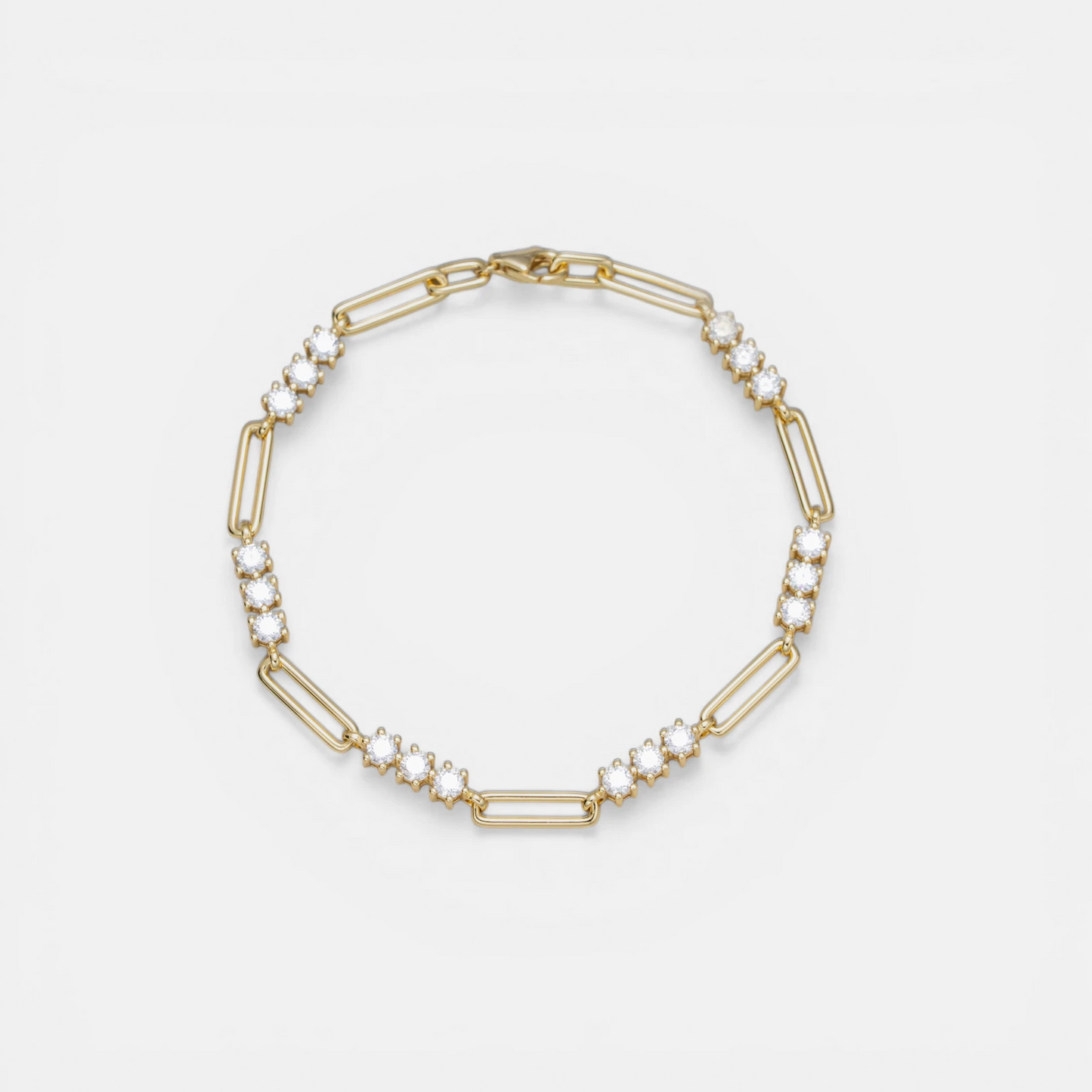 A gold link bracelet featuring alternating elongated oval links and smaller chain links embellished with clear round gemstones, displayed on a clean white background.