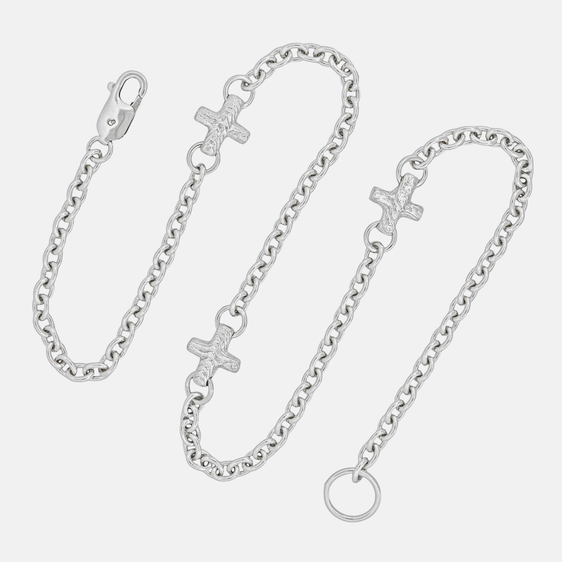 A silver chain bracelet with three small cross charms, a lobster clasp, and an extension ring, displayed on a light gray background.