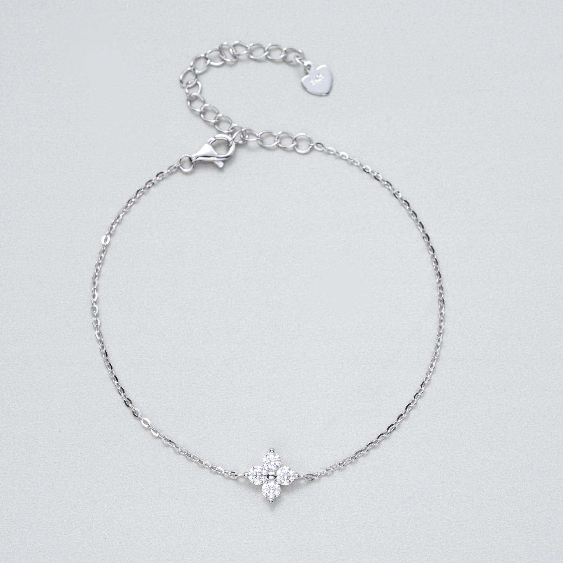 A delicate silver chain bracelet with a small silver cross charm set with clear stones, displayed on a light gray background.