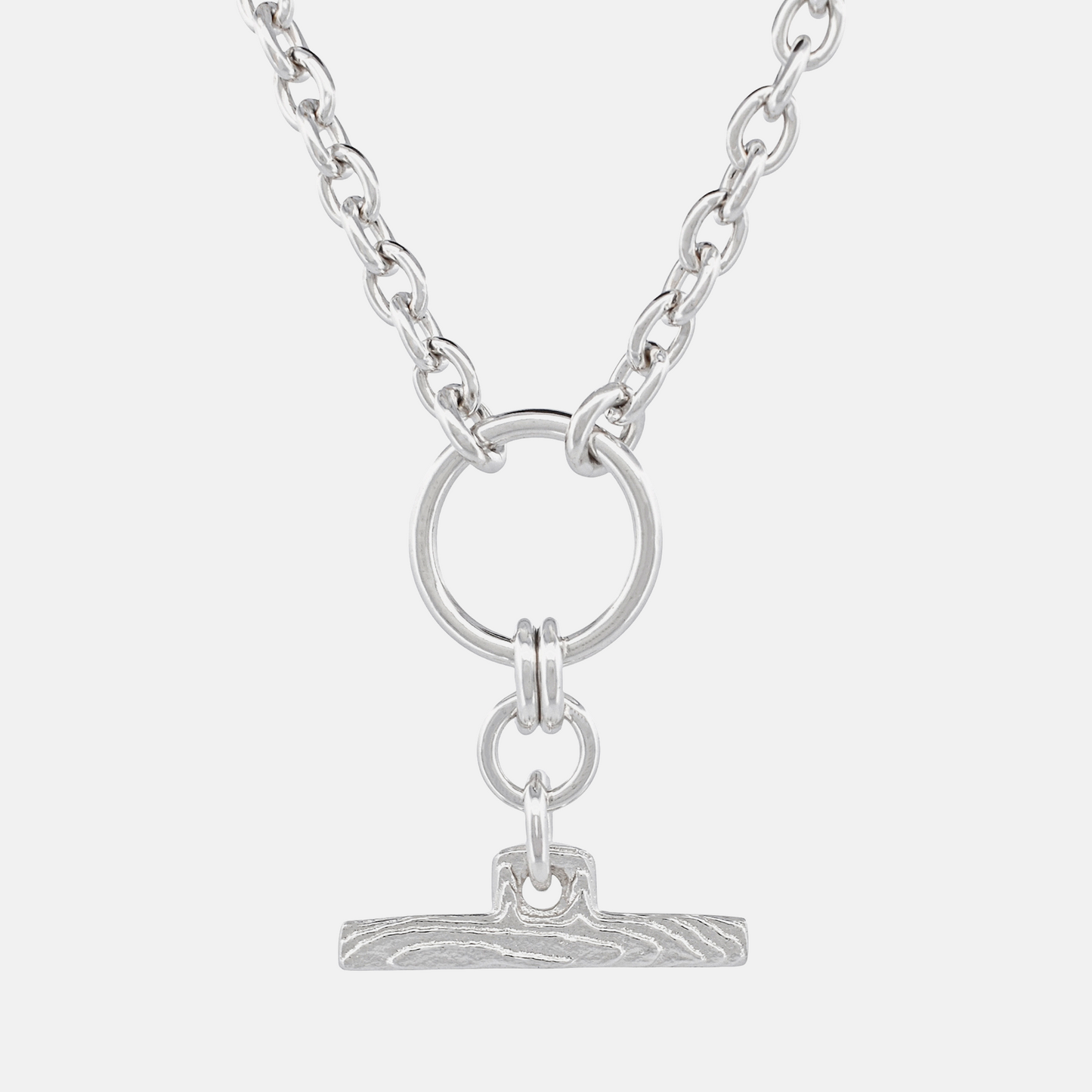 A silver-toned chain necklace featuring a circular ring and a small textured bar pendant, shown against a light gray background.