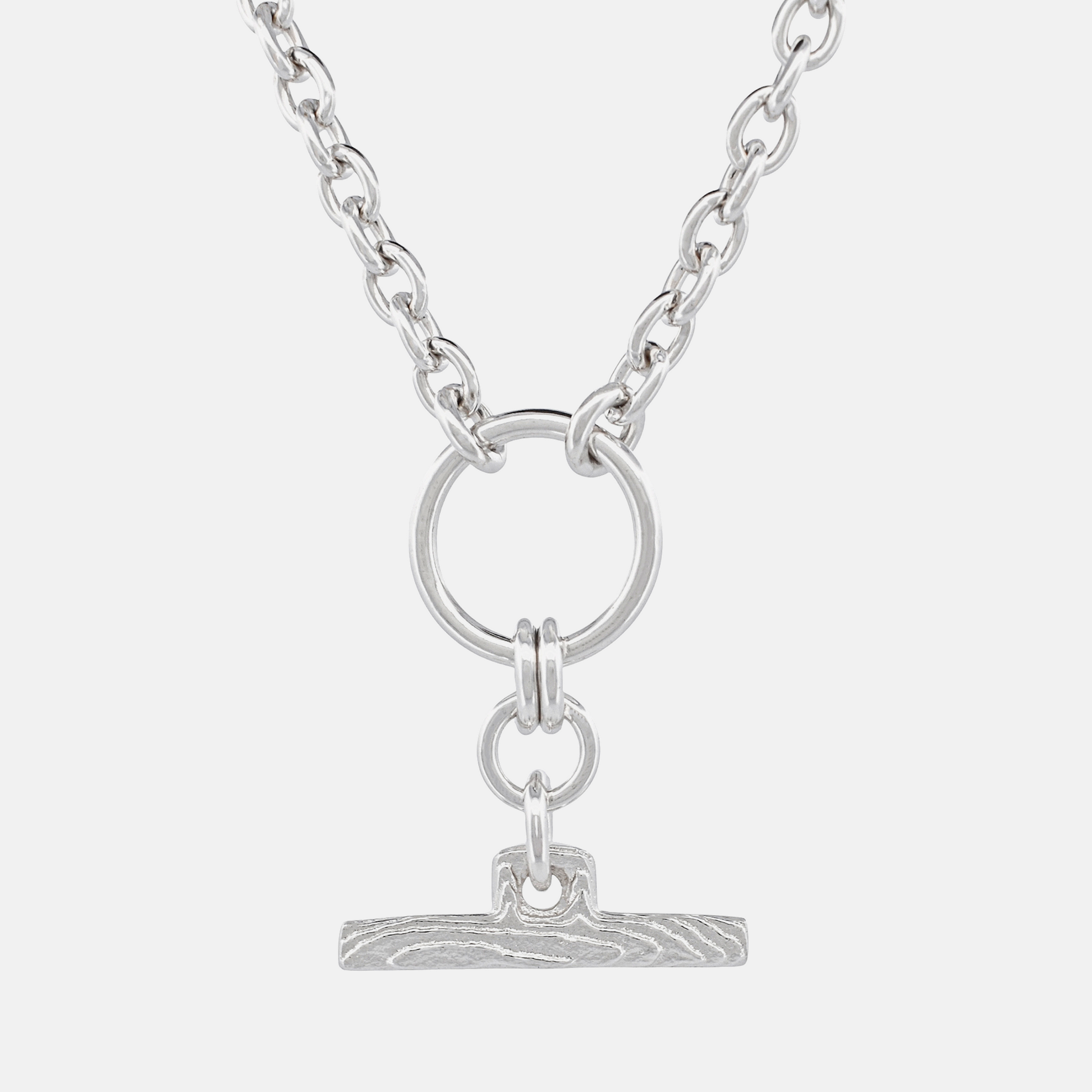 A silver-toned chain necklace featuring a circular ring and a small textured bar pendant, shown against a light gray background.