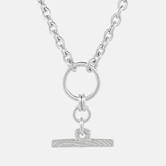 A silver-toned chain necklace featuring a circular ring and a small textured bar pendant, shown against a light gray background.