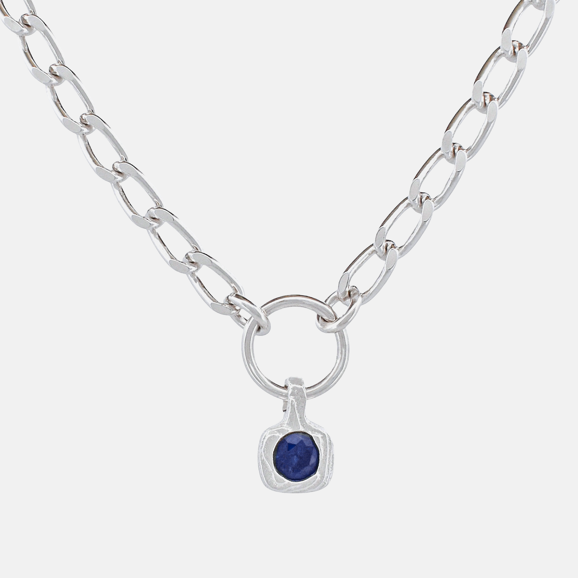 A silver chain necklace featuring a square bezel-set dark blue gemstone pendant, suspended from a circular ring on a light gray background.