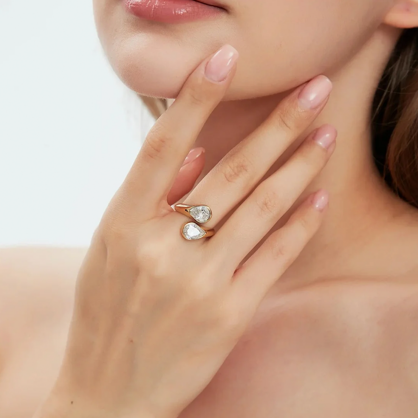 A close-up lifestyle shot of a model wearing a gold ring with two teardrop-shaped clear gemstones on her finger.