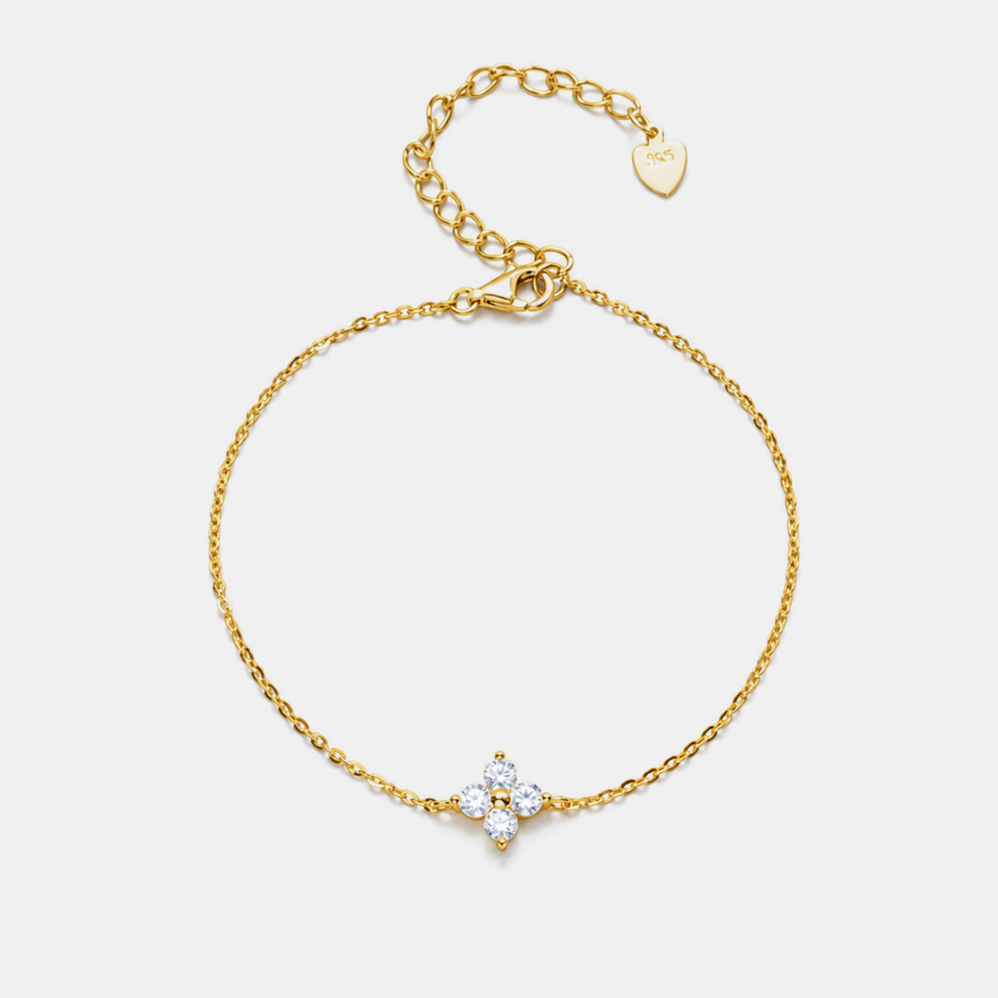 A delicate gold chain bracelet with a small four-petal flower charm set with clear stones, displayed on a light gray background.