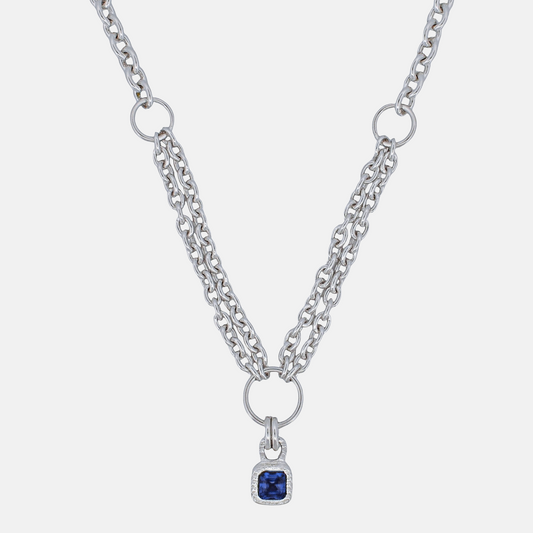 A silver-tone double-strand chain necklace featuring a central ring and a small square pendant with a deep blue gemstone surrounded by a clear crystal border, set against a light gray background.