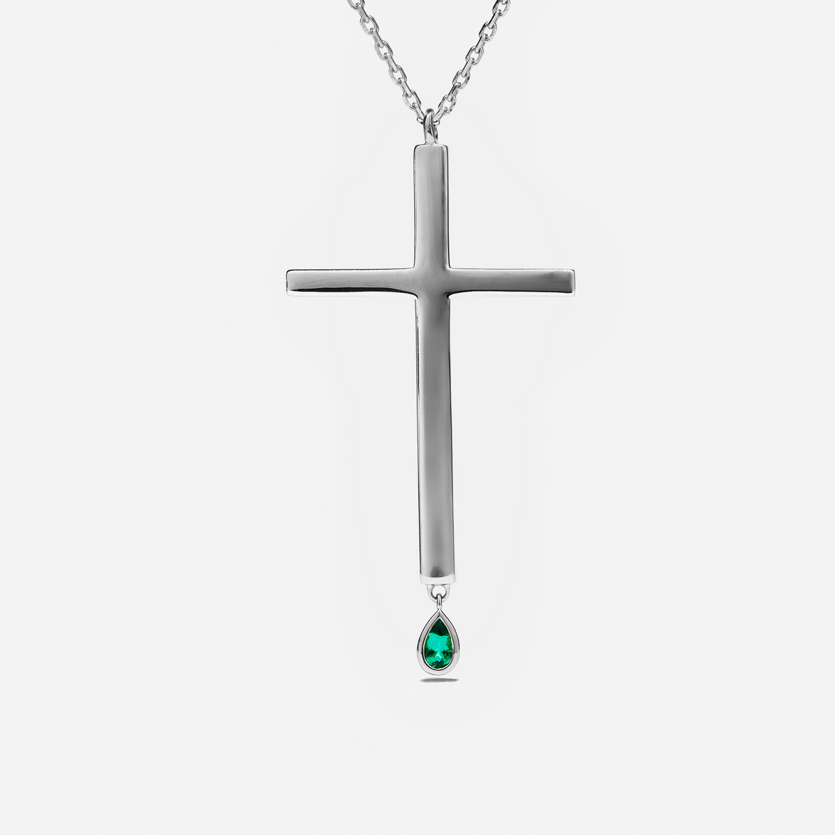 A silver cross pendant necklace with a teardrop-shaped green gemstone hanging from the bottom, shown against a light gray background.