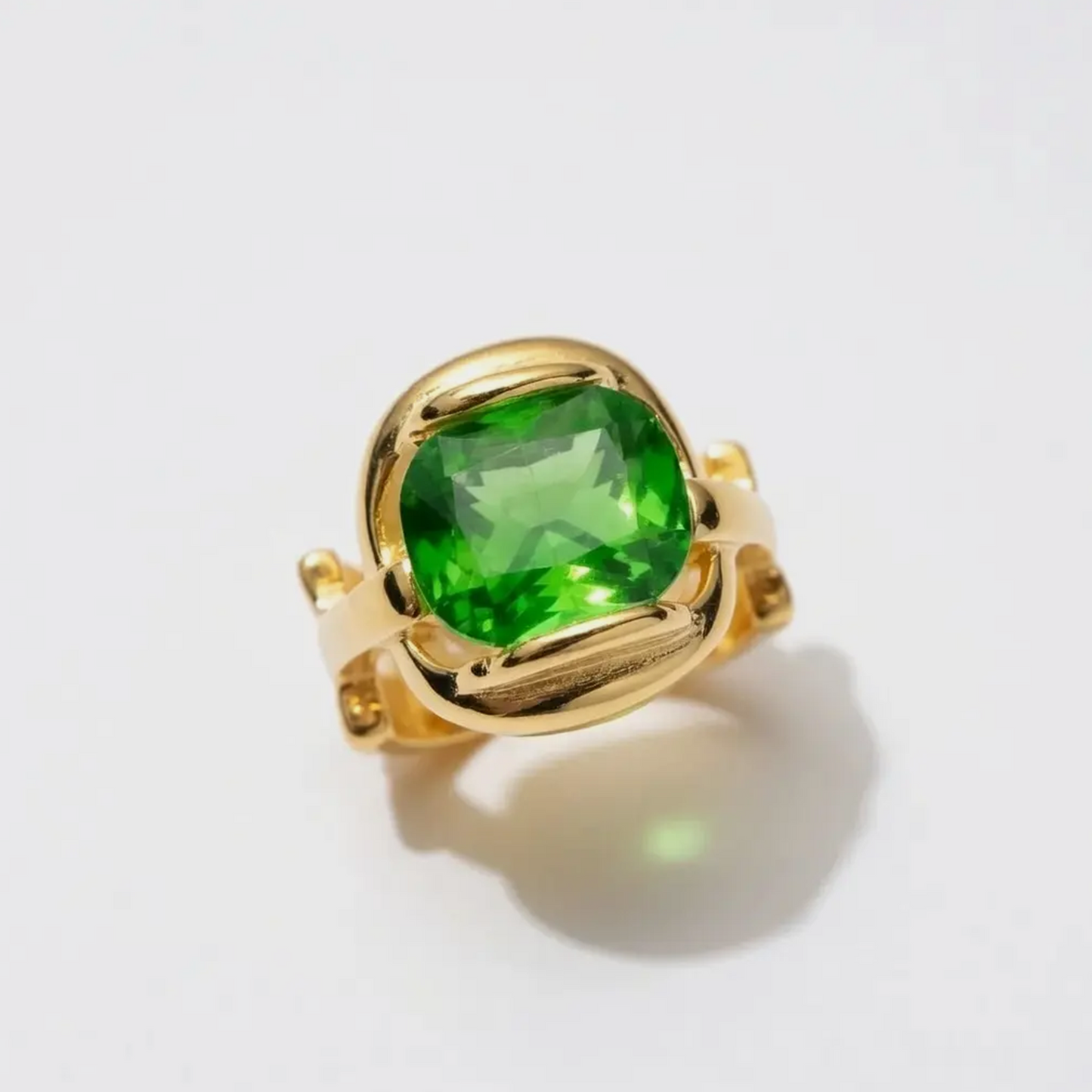 A cushion-cut emerald green gemstone ring set in a polished yellow gold bezel, photographed on a clean white background with a soft shadow.