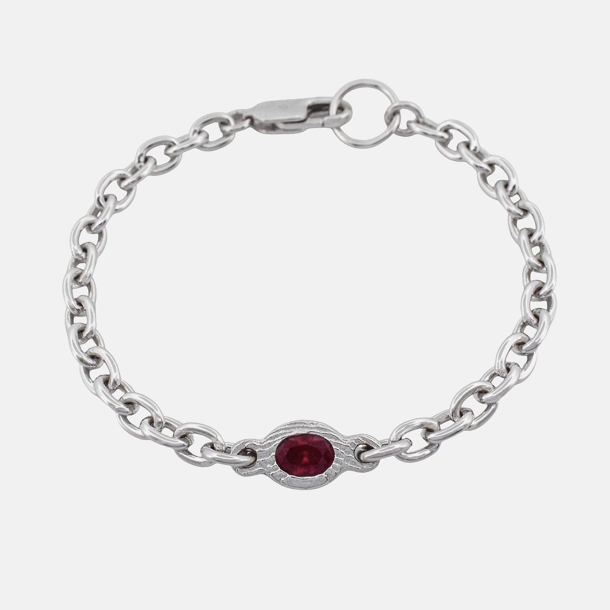 A silver chain bracelet featuring a central oval-cut red gemstone in a decorative silver bezel setting, shown on a light gray background.
