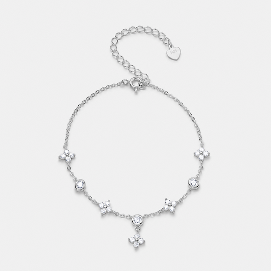 A delicate silver chain bracelet featuring five small floral star motifs and a central round clear stone, with an adjustable lobster clasp and heart-shaped tag, shown on a light gray background.