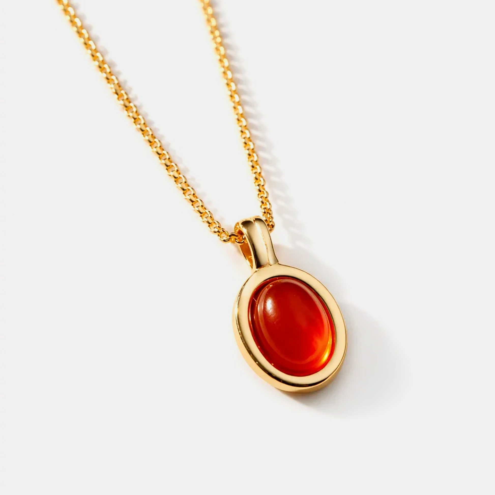 A gold chain necklace with an oval pendant featuring a smooth, polished red cabochon gemstone, set against a clean light gray background.