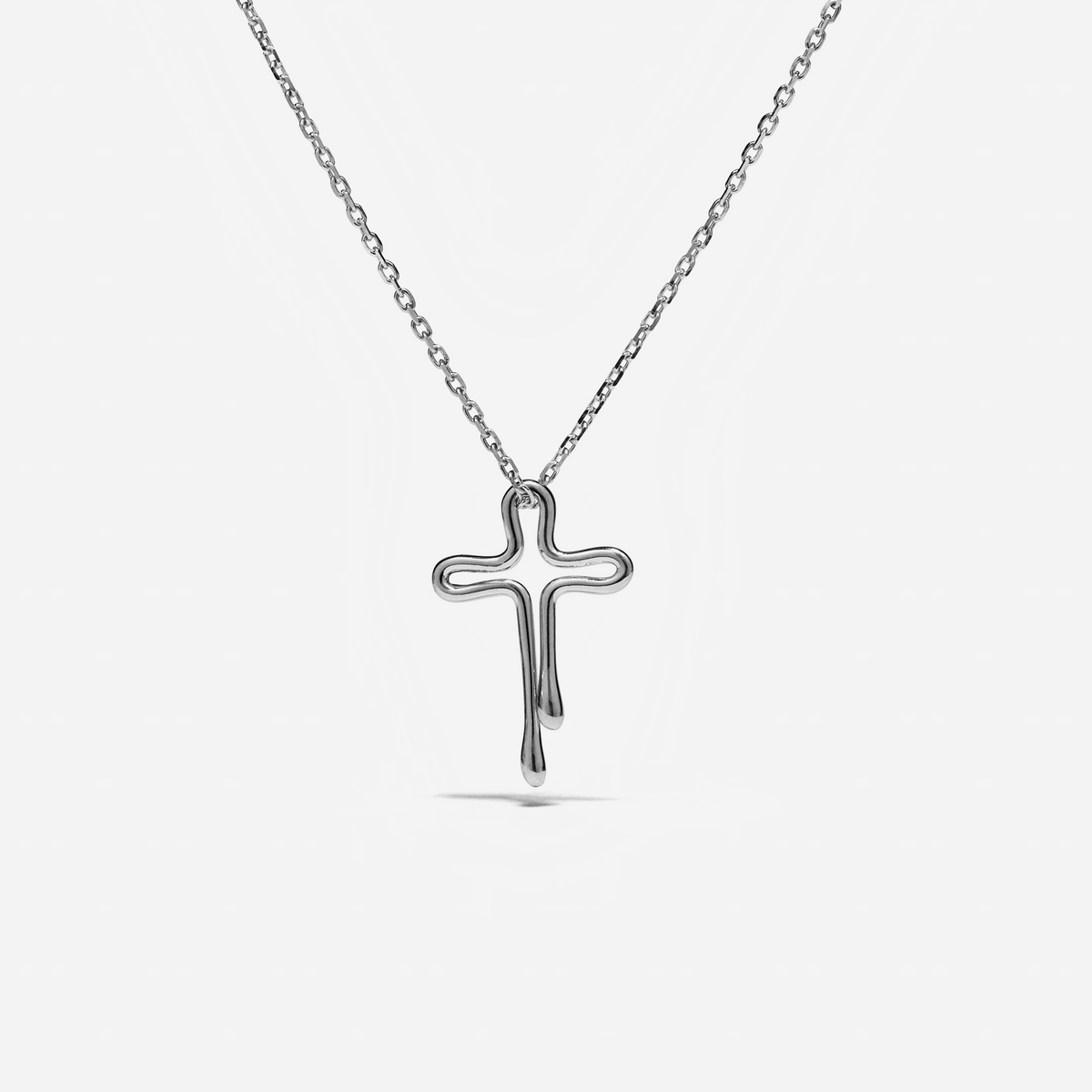A polished silver cross pendant necklace with a dripping design, suspended from a delicate silver cable chain against a light gray background.