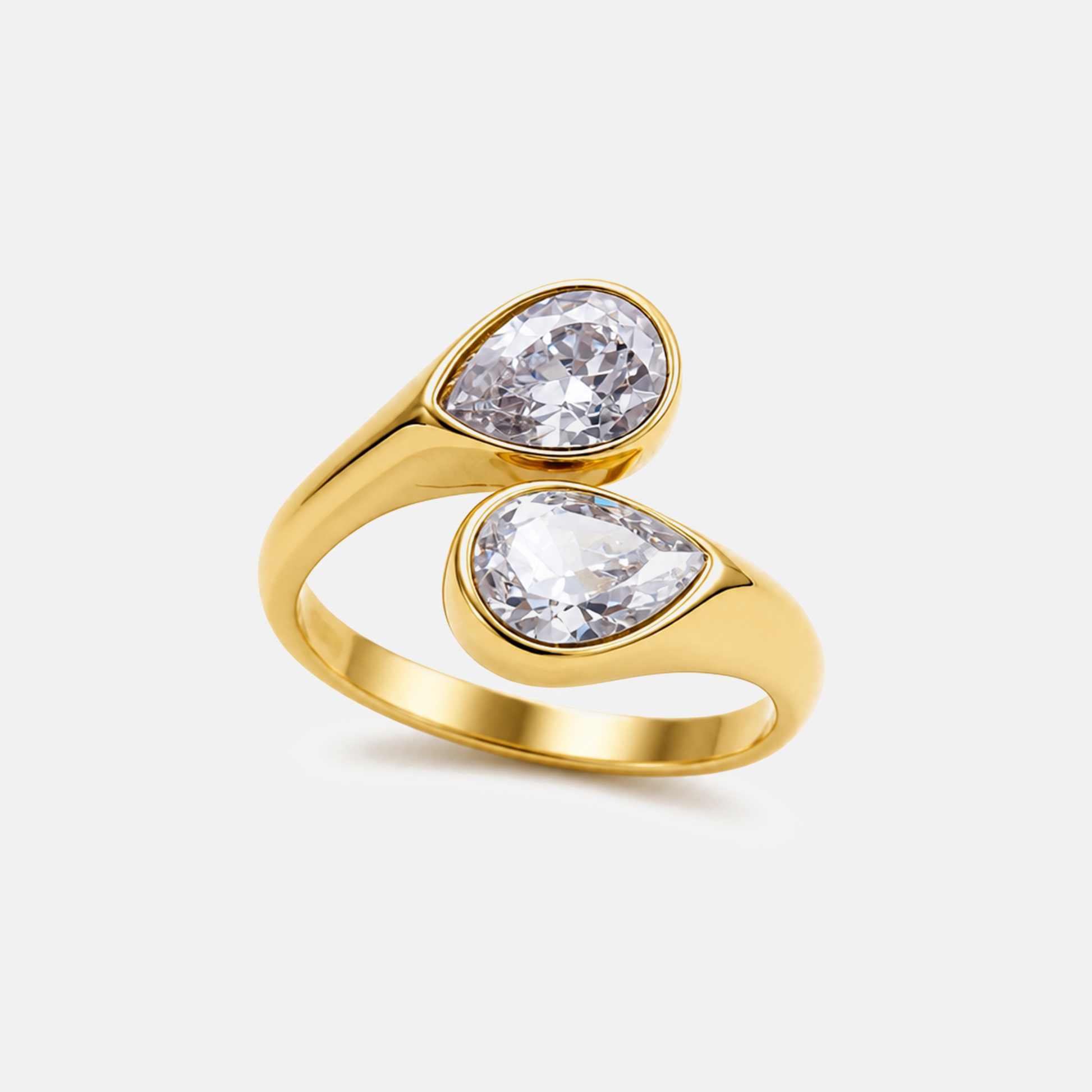 A gold ring featuring two pear-cut clear gemstones in a wrap-around design, set against a clean off-white background.