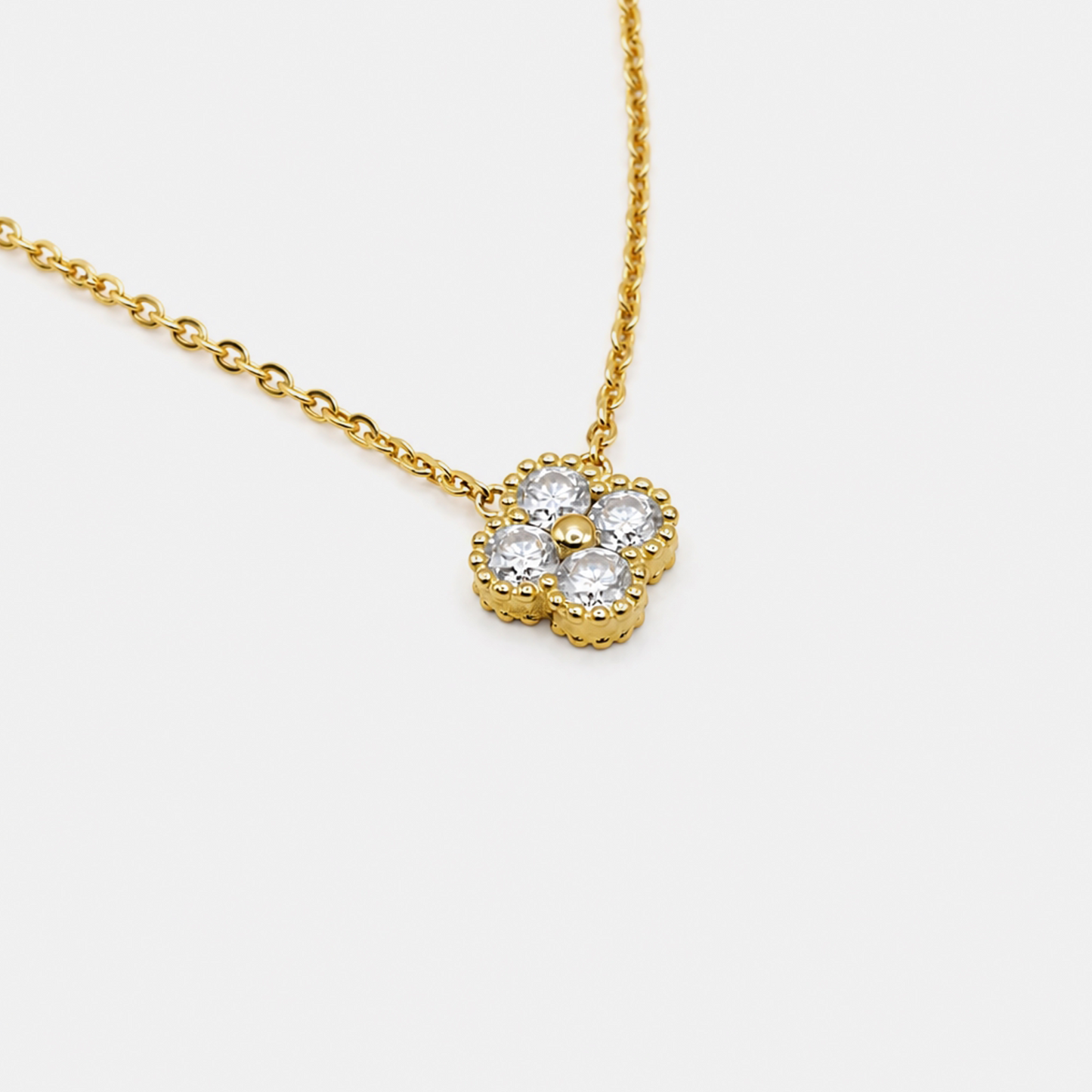 A gold chain necklace with a flower-shaped pendant featuring five clear round-cut stones, shown on a light gray background.