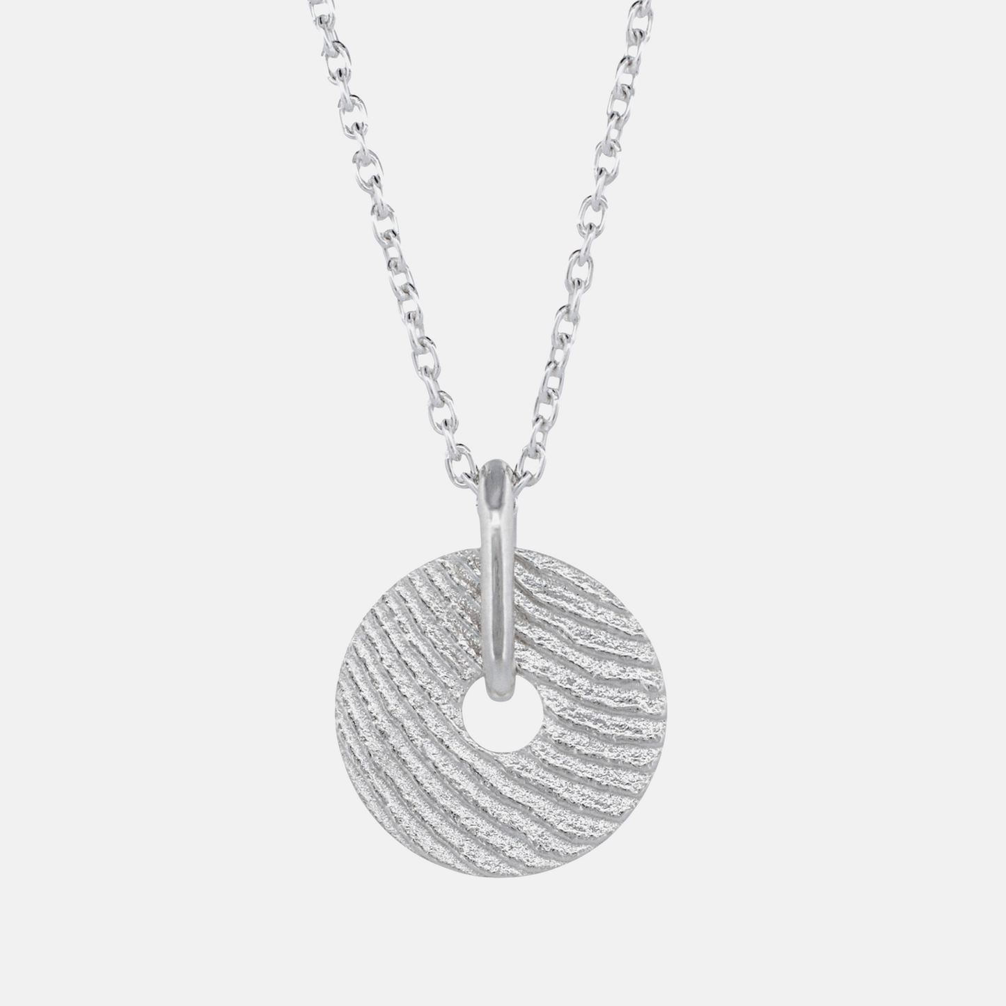 A silver necklace featuring a textured circular disc pendant with a central hole, suspended from a classic curb chain against a light gray background.