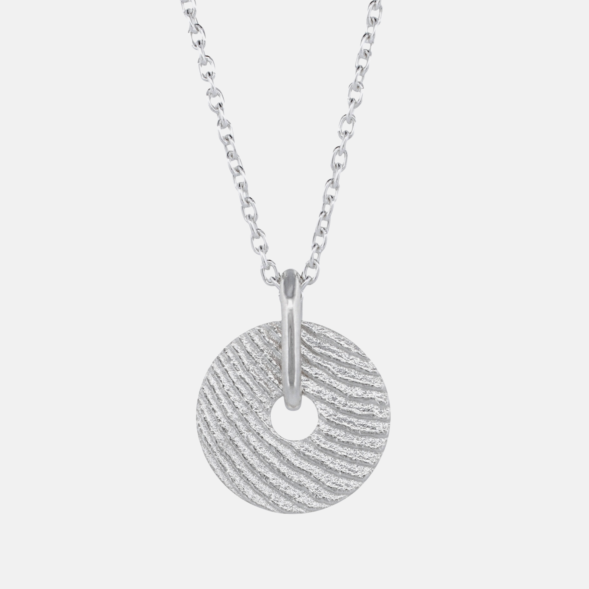 A silver necklace featuring a textured circular disc pendant with a central hole, suspended from a classic curb chain against a light gray background.