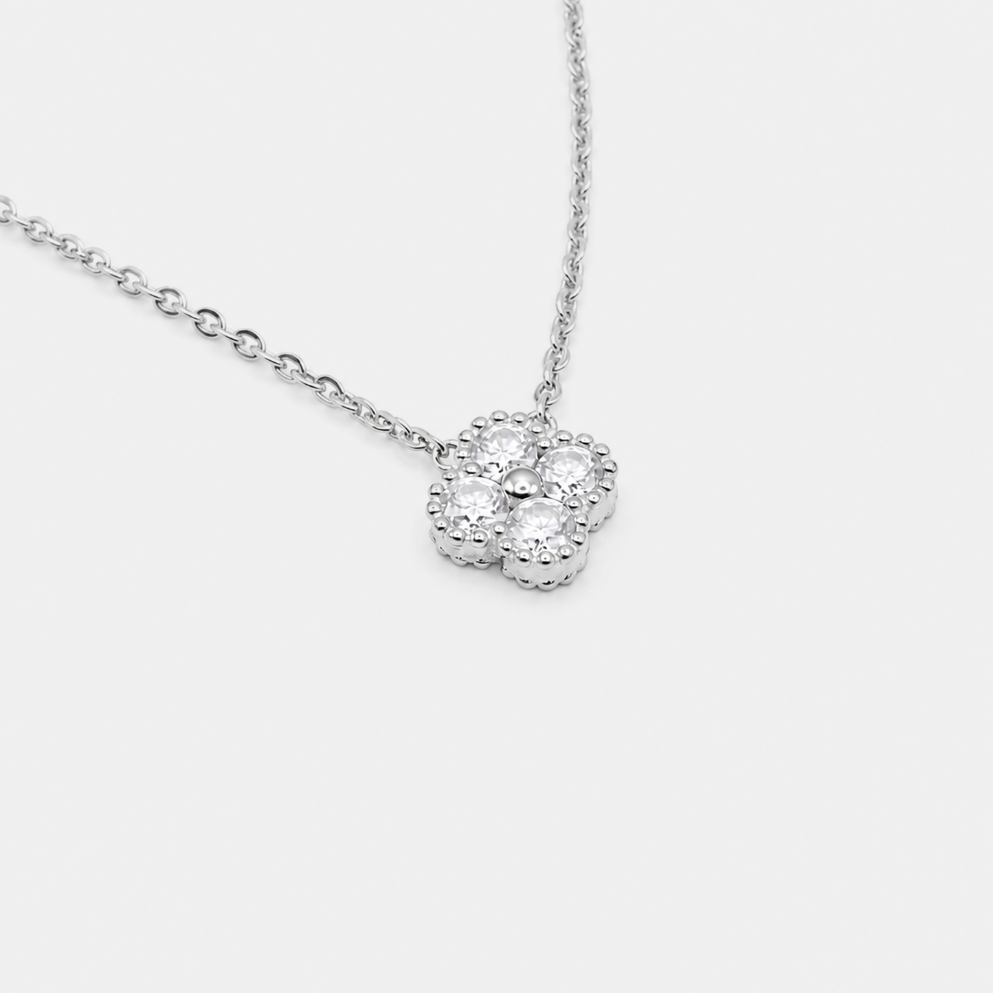 A silver-tone floral pendant necklace featuring a central round clear gemstone surrounded by a halo of smaller stones, suspended from a delicate link chain against a light gray background.