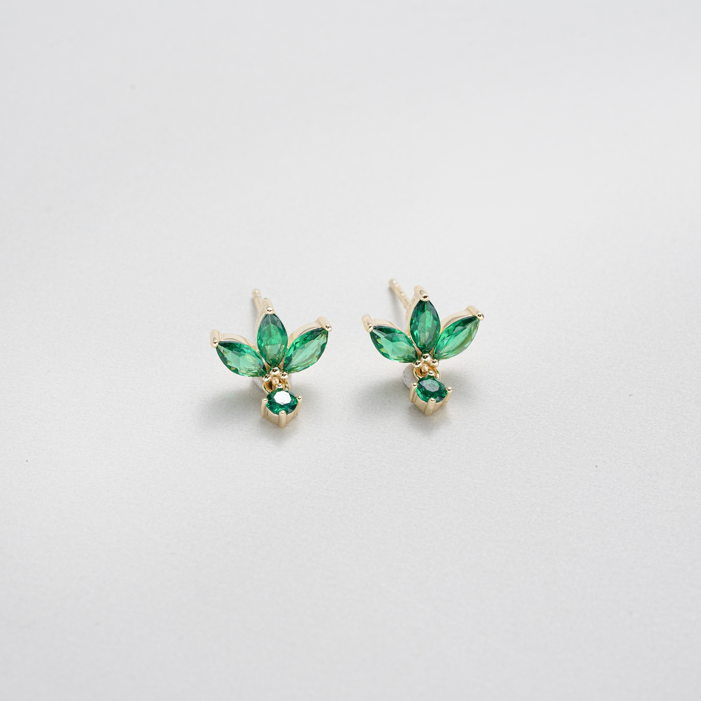 A pair of gold stud earrings featuring marquise-cut green gemstones arranged in a leaf-like cluster with a small round green stone below, photographed on a clean white background.