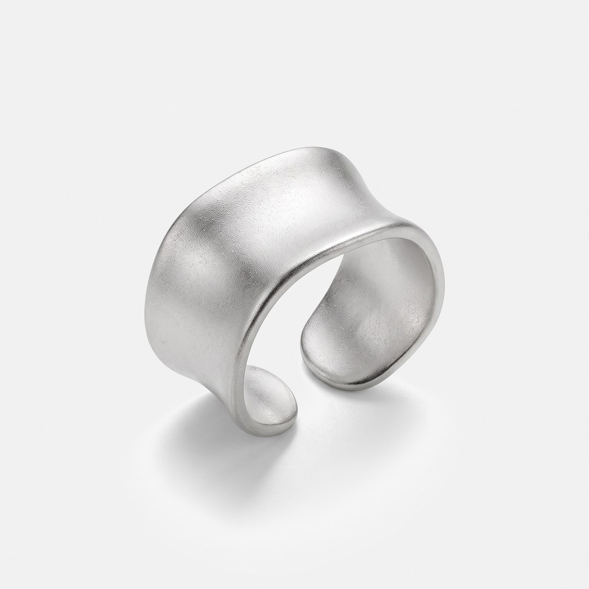A wide, open cuff ring in matte silver-tone metal with a smooth, organic wavy silhouette, photographed on a clean light gray background.