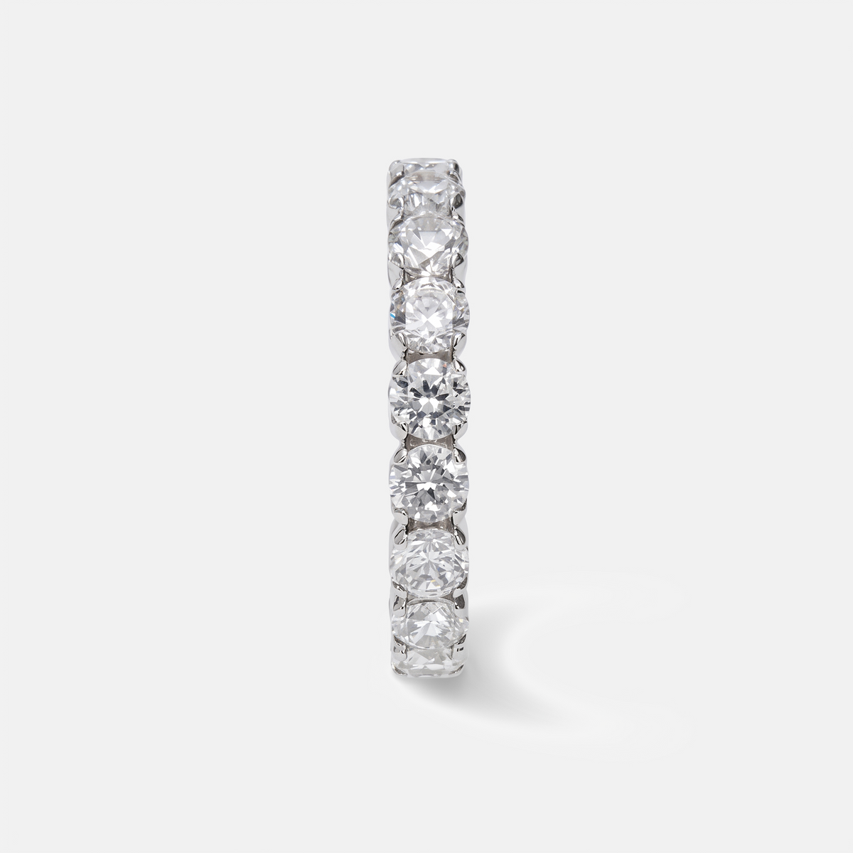 A slim silver-tone eternity band ring featuring a row of round brilliant-cut clear gemstones, shown on a clean light gray background.