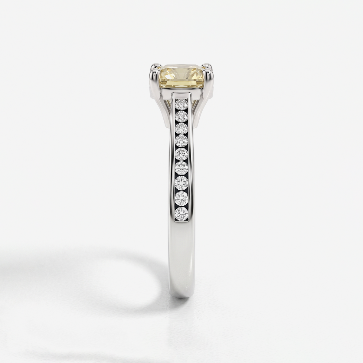 A close-up studio shot of a silver-toned ring featuring a rectangular yellow gemstone in a prong setting and a channel of small clear stones along the band, set against a clean white background.