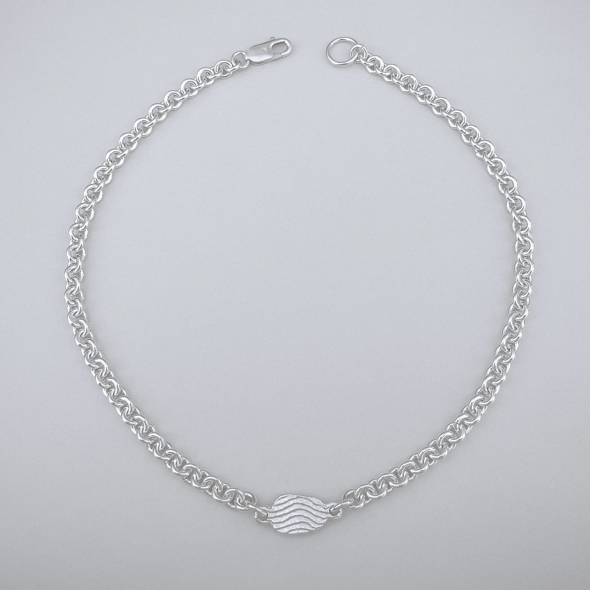 Silver chain bracelet with a wave design on a light gray background