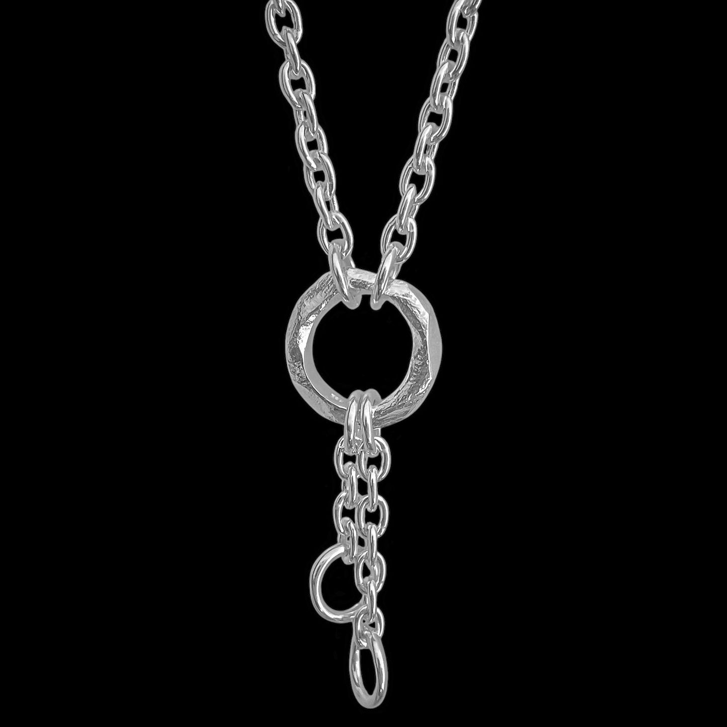 A silver chain necklace featuring a textured circular ring clasp with a short drop chain and a small hanging ring, shown against a solid black background.