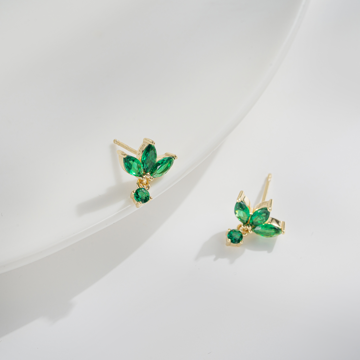 A pair of gold-tone butterfly stud earrings with marquise-cut and round green gemstones, displayed on a clean white surface.