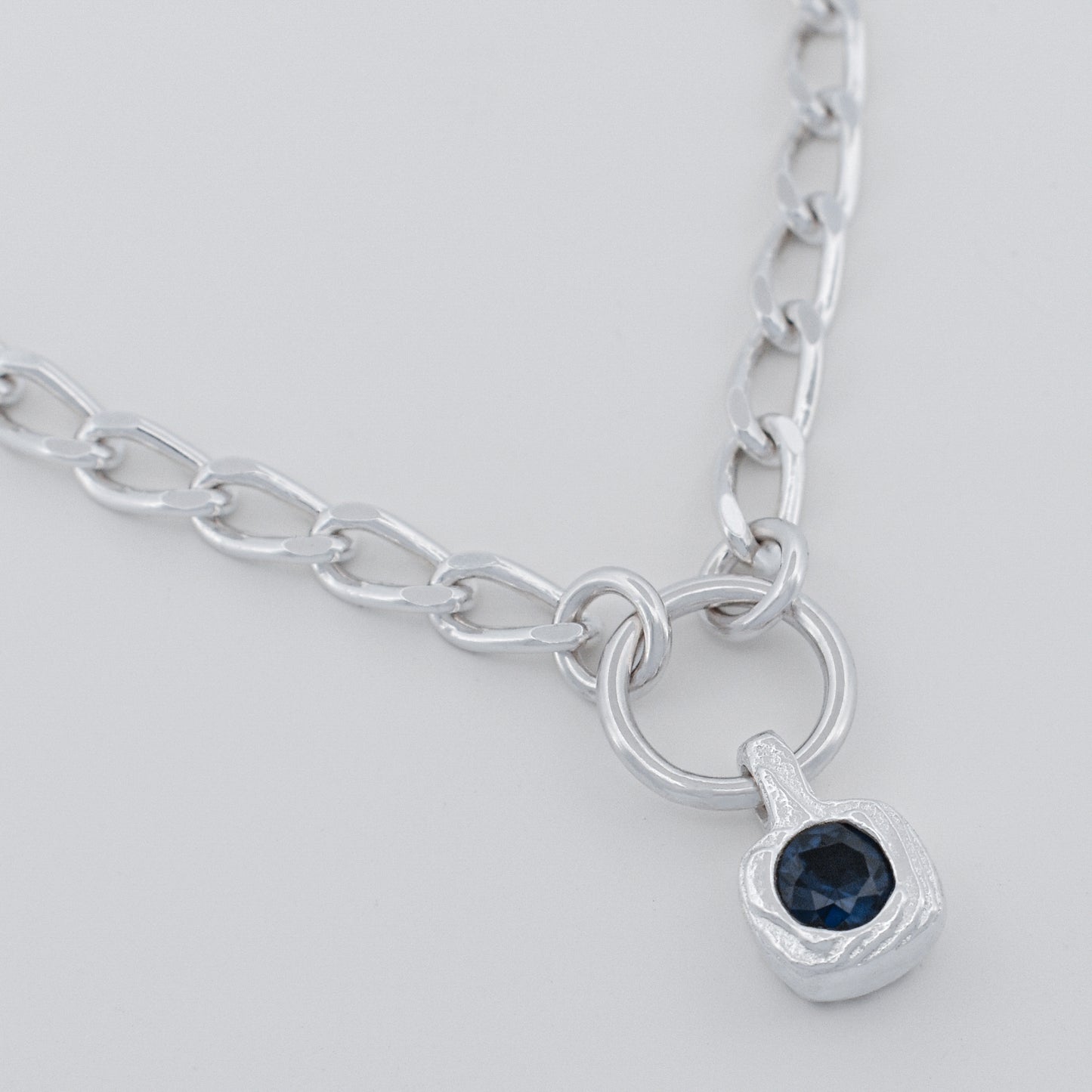 Silver necklace with a blue gemstone pendant on a light gray background