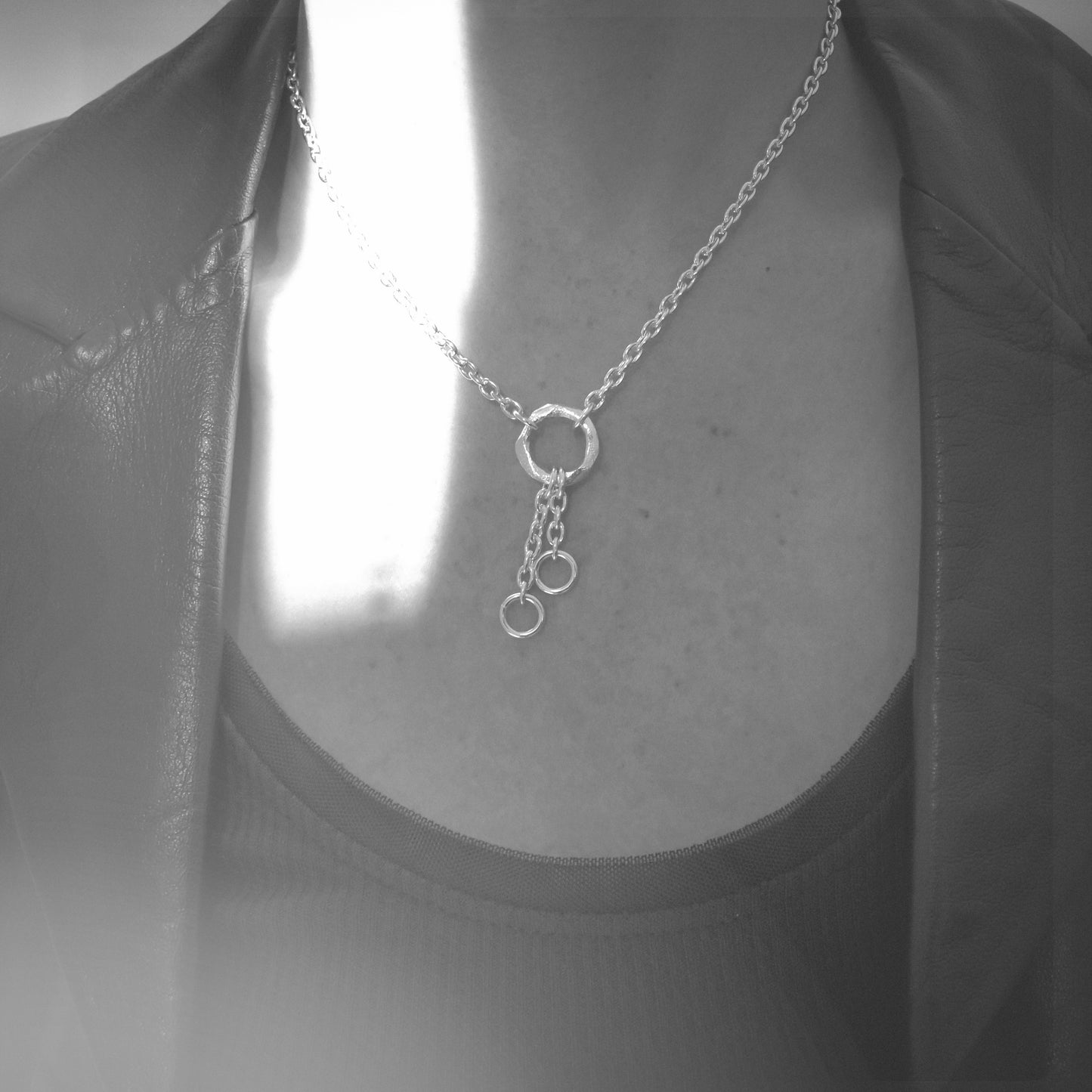 A silver necklace with three interlocking circular ring pendants on a delicate chain, shown worn on a mannequin or model's neck over a dark top and jacket.