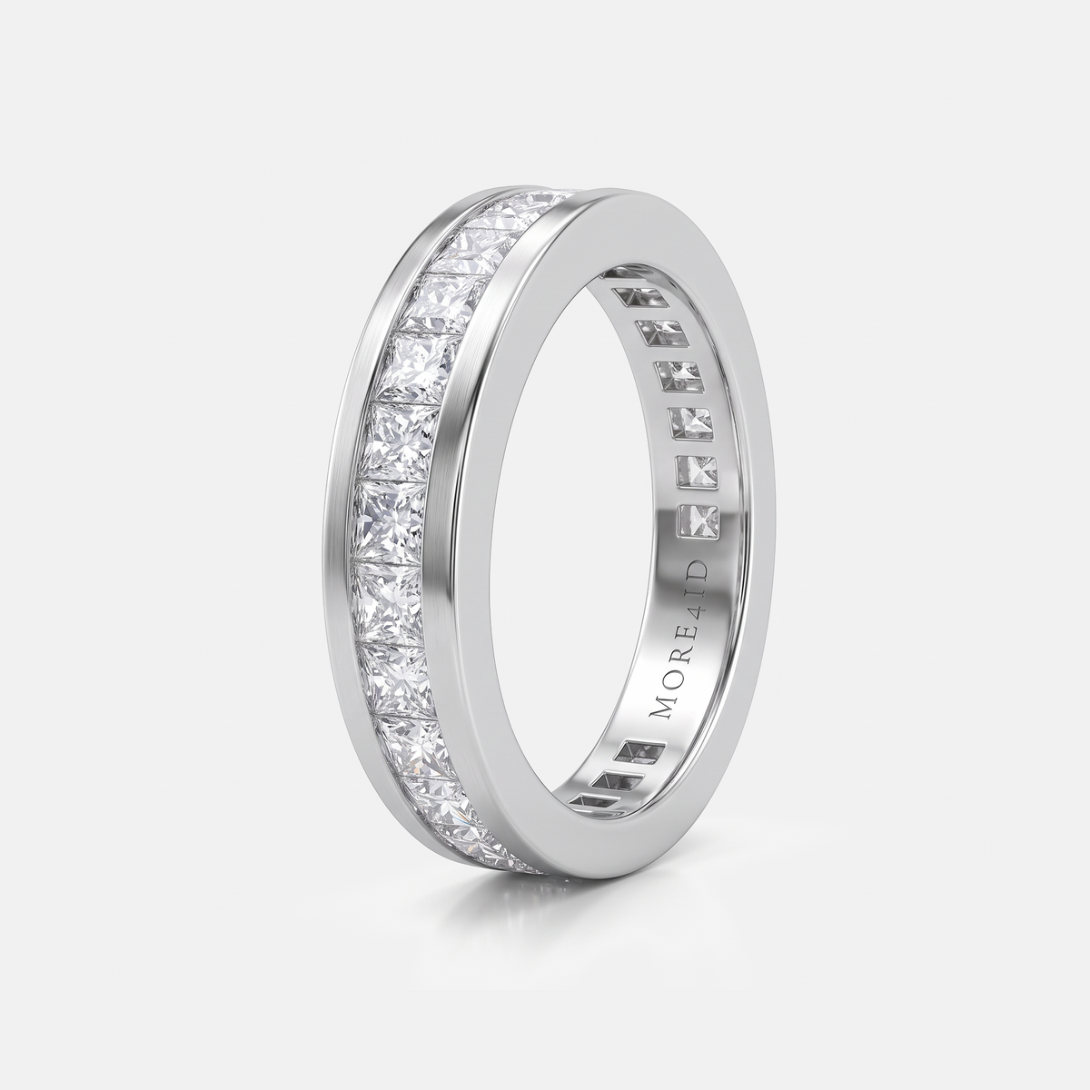 A silver-colored eternity ring with a channel-set row of clear princess-cut diamonds on a light gray background. The brand name 'MORE & JUD' is engraved on the inside of the band.