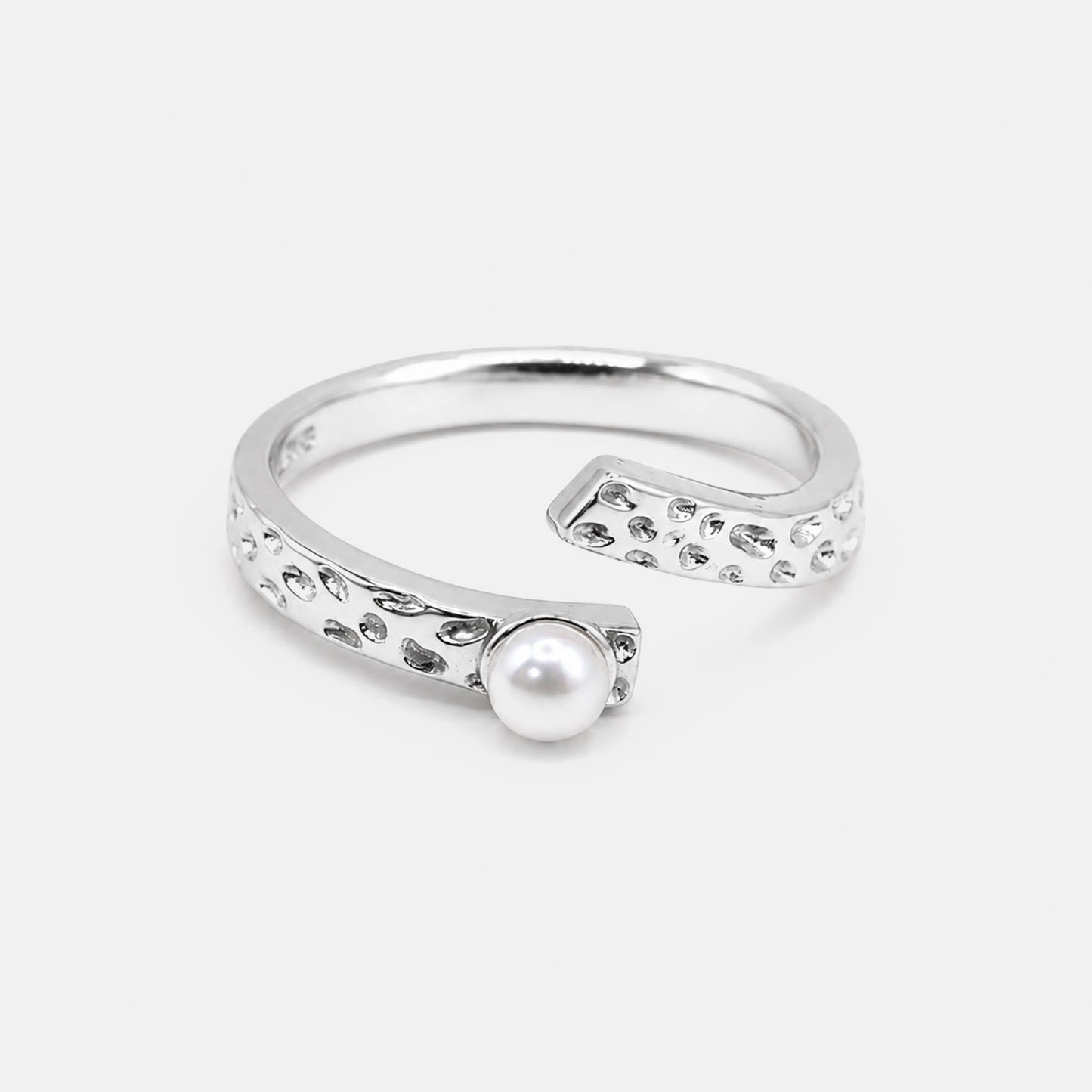 A silver open cuff ring featuring a textured, dotted border and a single white pearl set in the center, photographed on a light gray background.