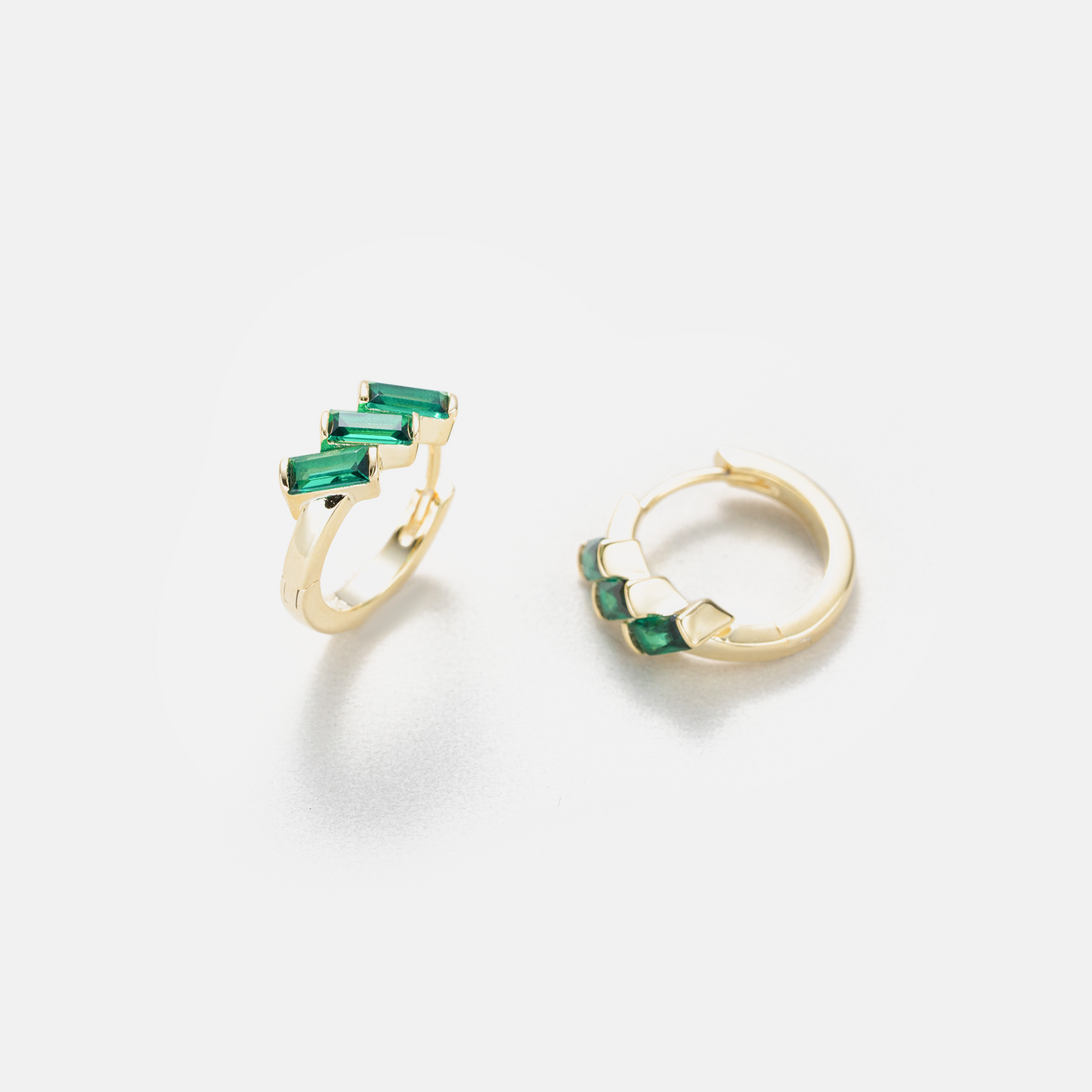 A pair of gold hoop earrings with small green gemstone accents, shown on a clean white background.