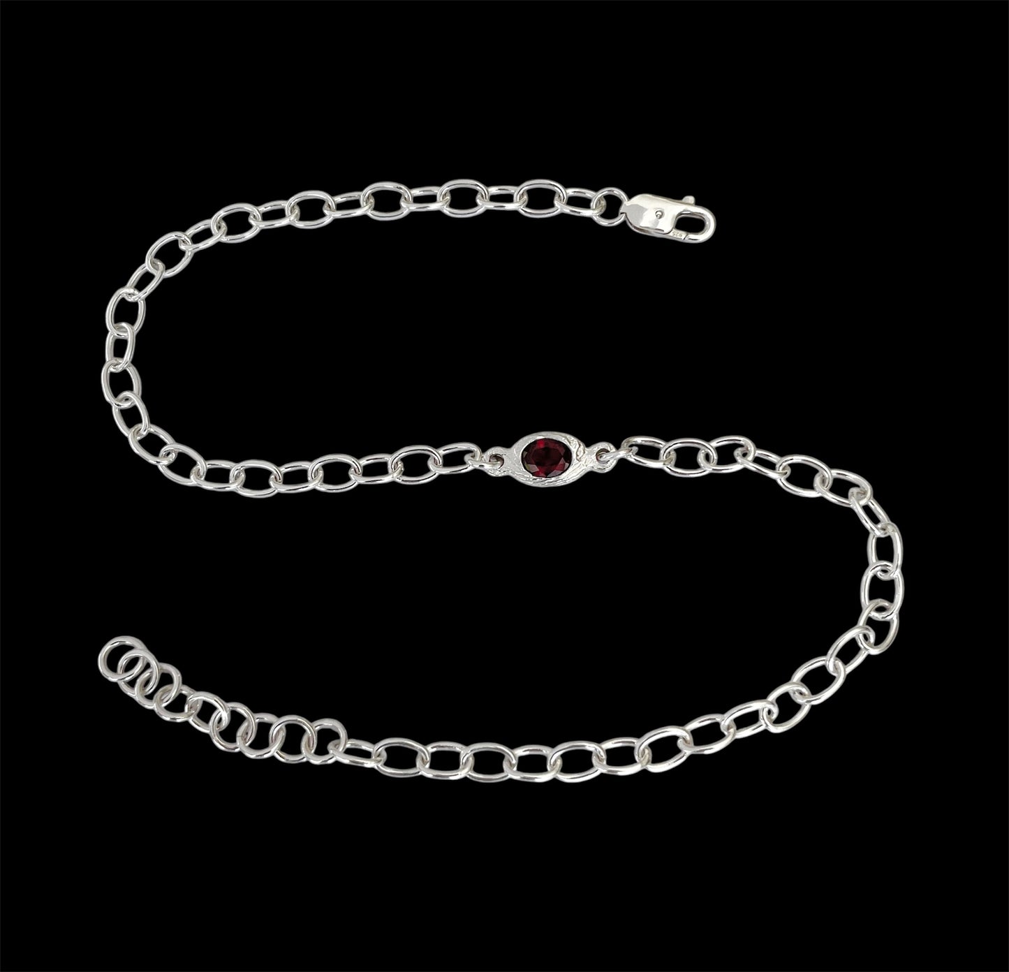 Silver chain bracelet with a red gemstone on a black background