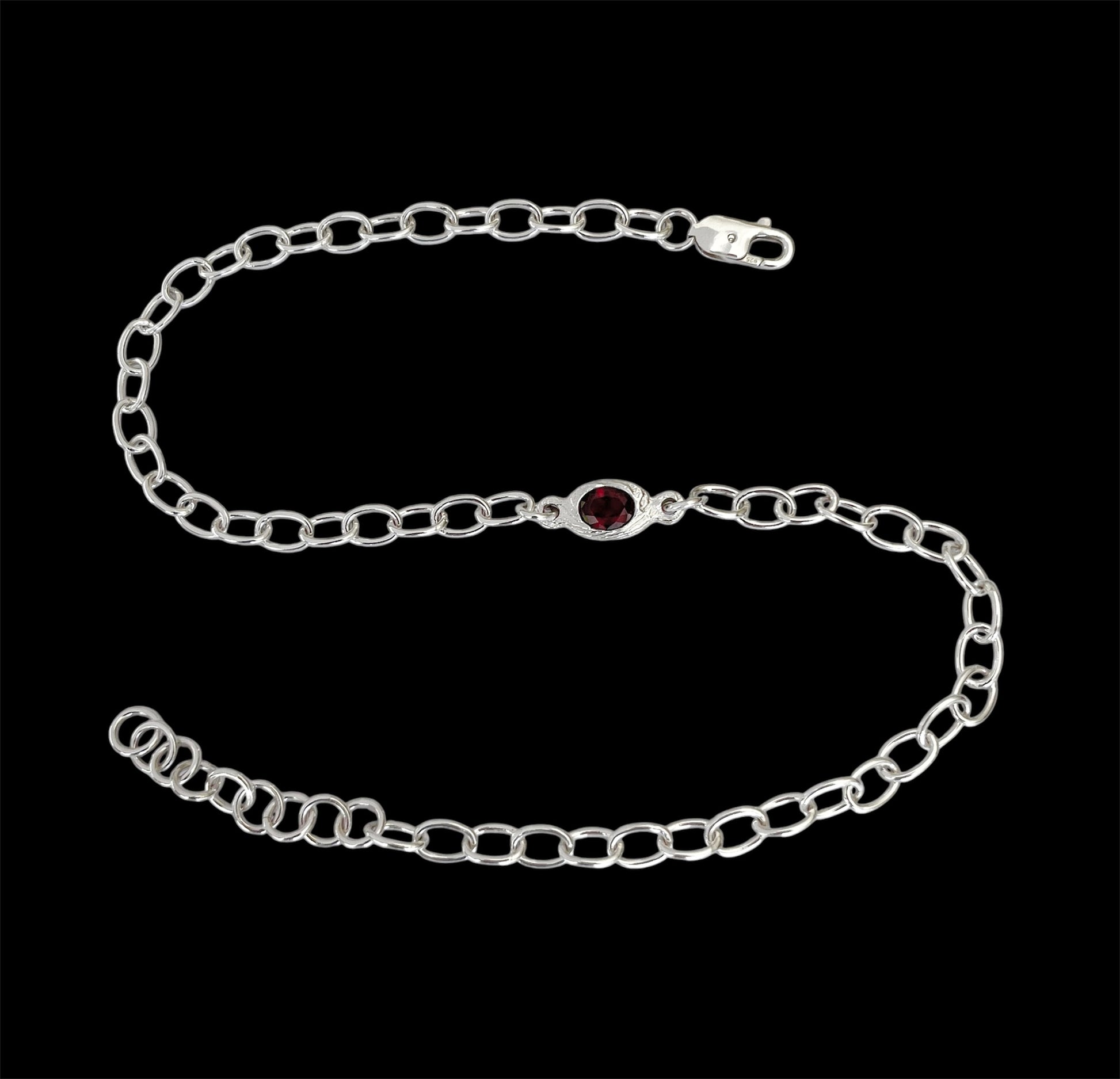Silver chain bracelet with a red gemstone on a black background