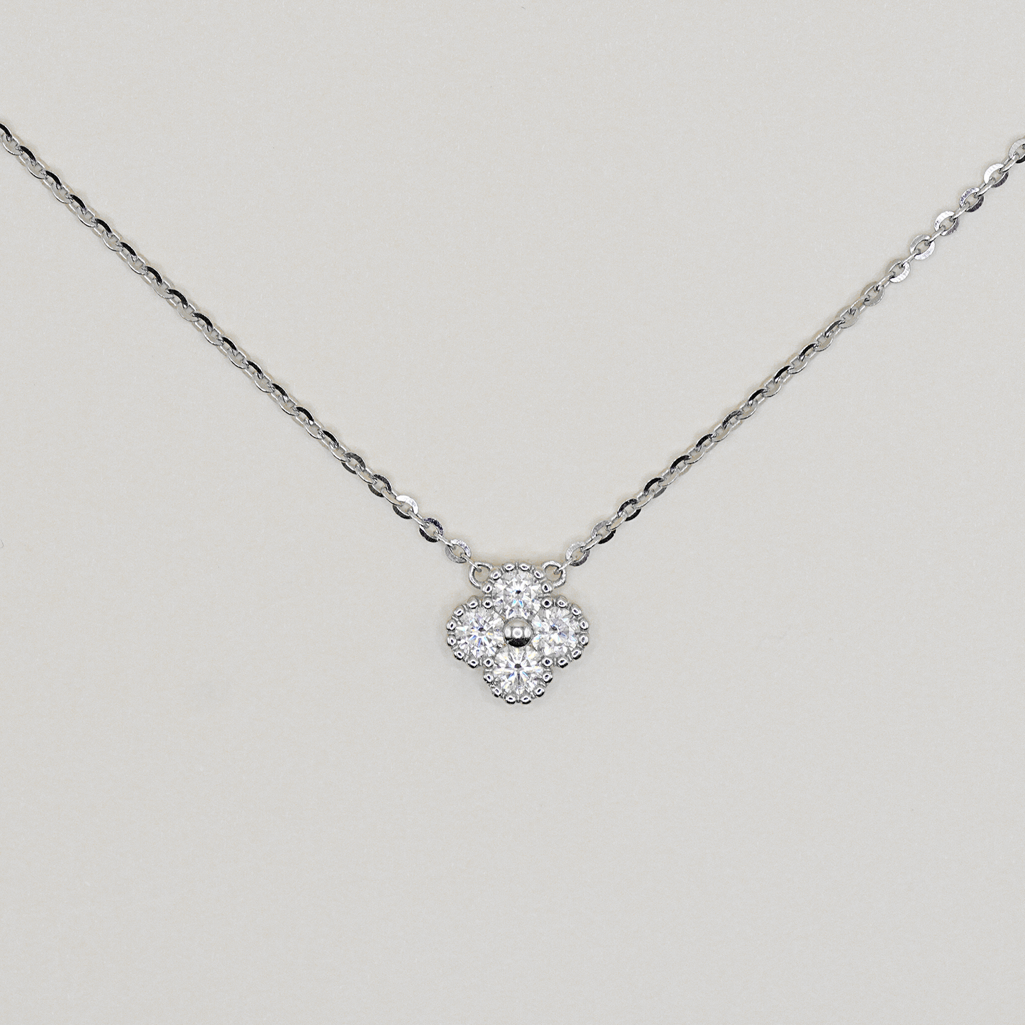 A delicate silver chain necklace with a small four-petal flower pendant paved with clear stones, displayed against a light gray background.