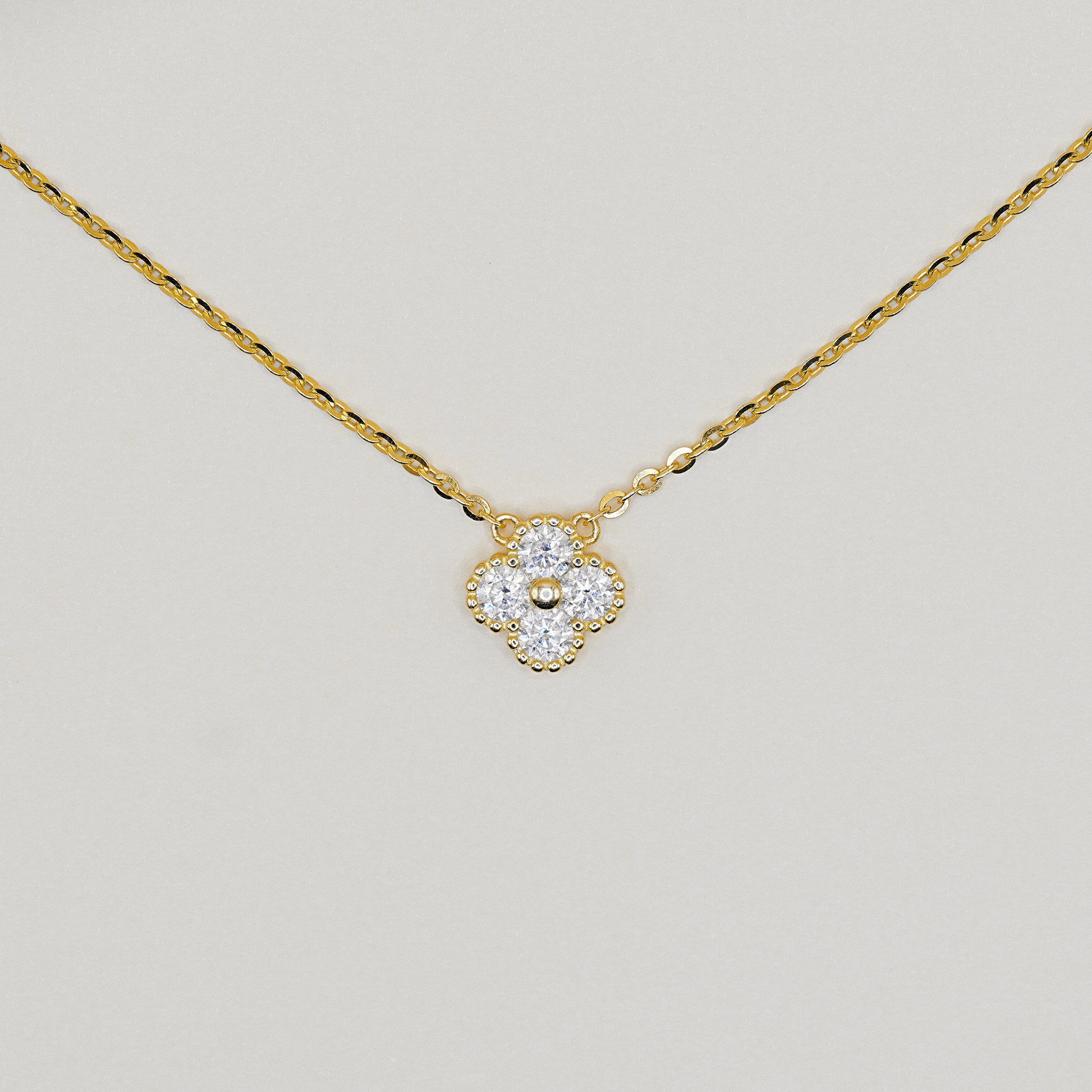 A delicate yellow gold chain necklace with a small four-petal flower pendant. The pendant is set with clear gemstones and a central gold bead, photographed against a neutral light gray background.